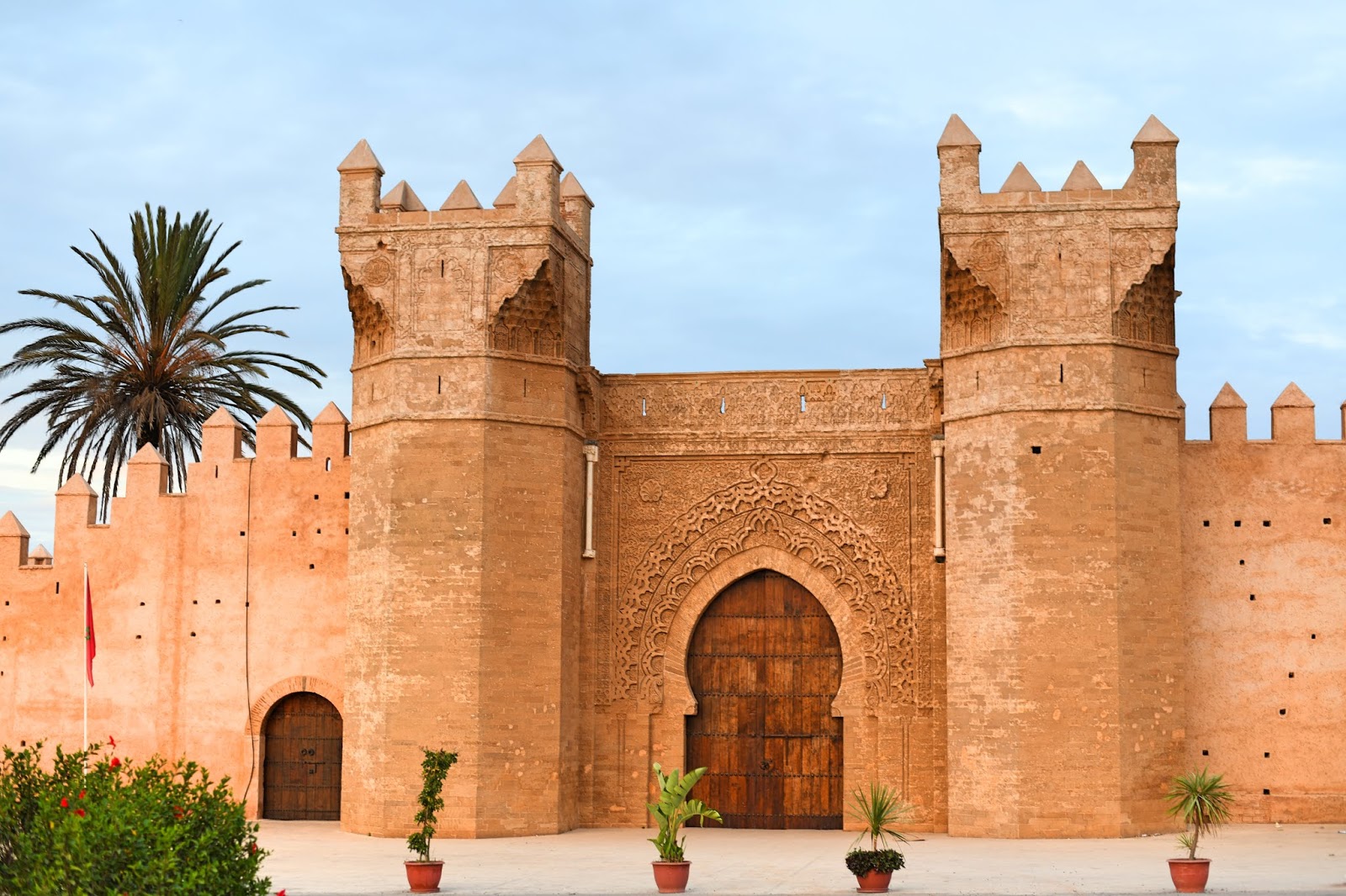 Moroccan Oudaya kasbah in rabat with ornate arched door, stone walls, and palm tree during a day visit withMoroccan Guides Travel.