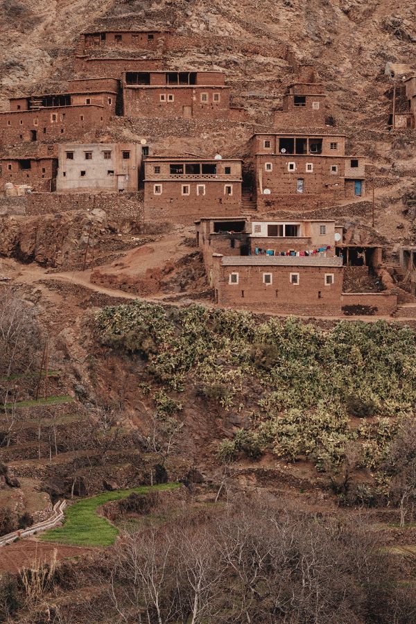 Traditional mud brick village nestled on rocky mountainside in Imlil of the high atlas of Mororccoc with green valley below