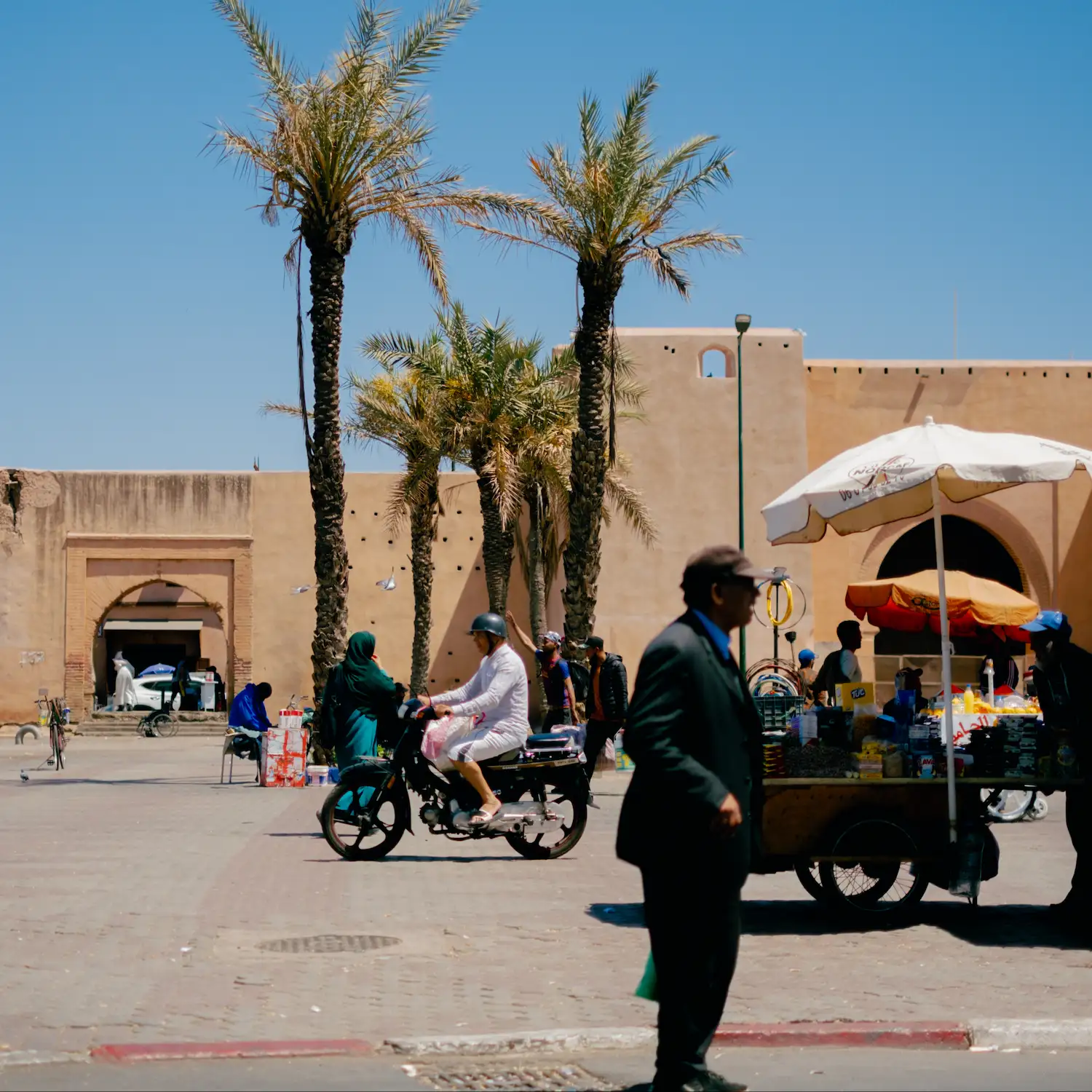 Moroccan street scene with palm trees, market stalls, and people on bicycles in the red city of marrakech