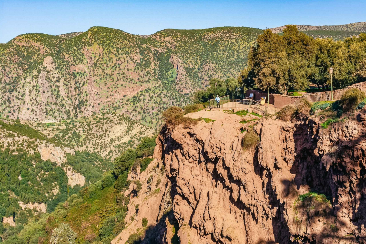Steep rocky cliff overlooks lush green valley of Ouzoud with mountain landscape during a tour with Moroccan Guides Travel