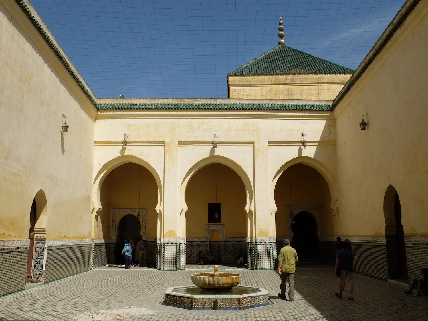 Moroccan Mausoleum of Moulay Idriss with ornate fountain, arched doorways, and green-tiled roof in Fes during a tour with Moroccan Guides Travel