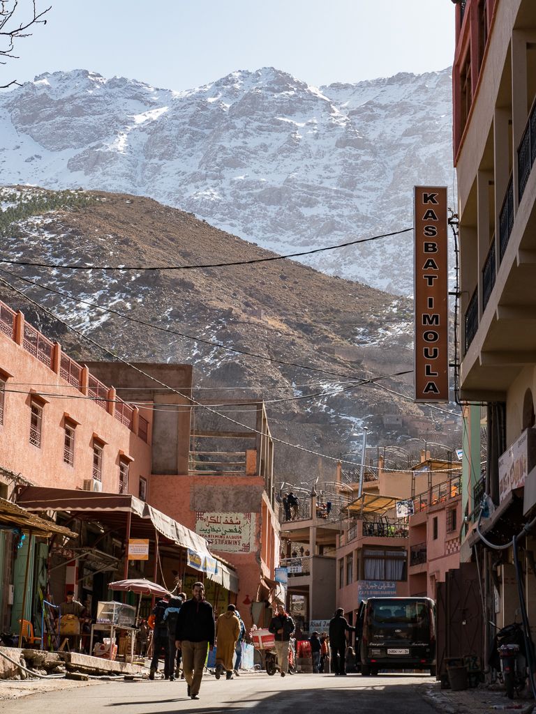 Snowy mountain backdrop over bustling street in Moroccan mountain town during a tour with Moroccan Guides Travel