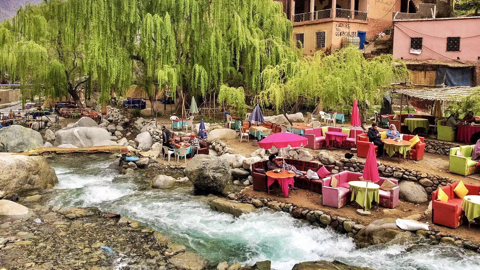 Colorful riverside cafe in Ourika Village  with pink umbrellas nestled among willow trees and rocks