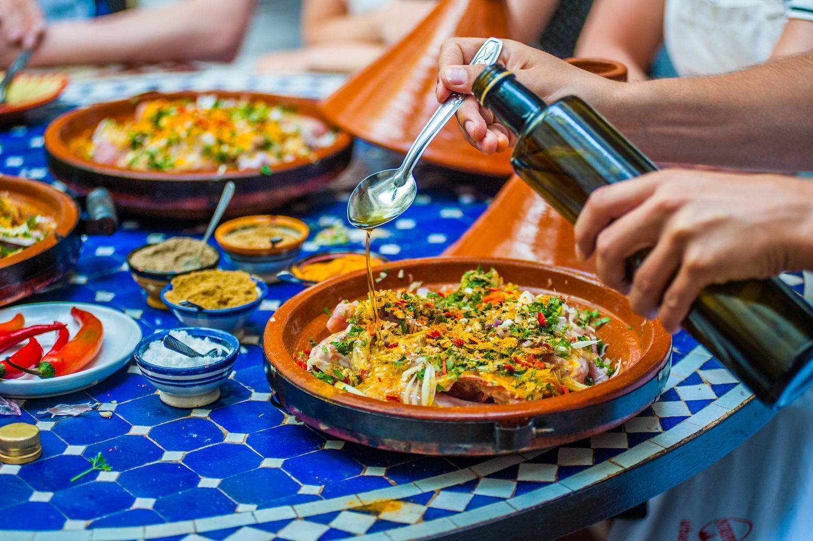 Moroccan tagine being prepared with spices and olive oil on blue mosaic table during a coocking class with Moroccan Guides Travel