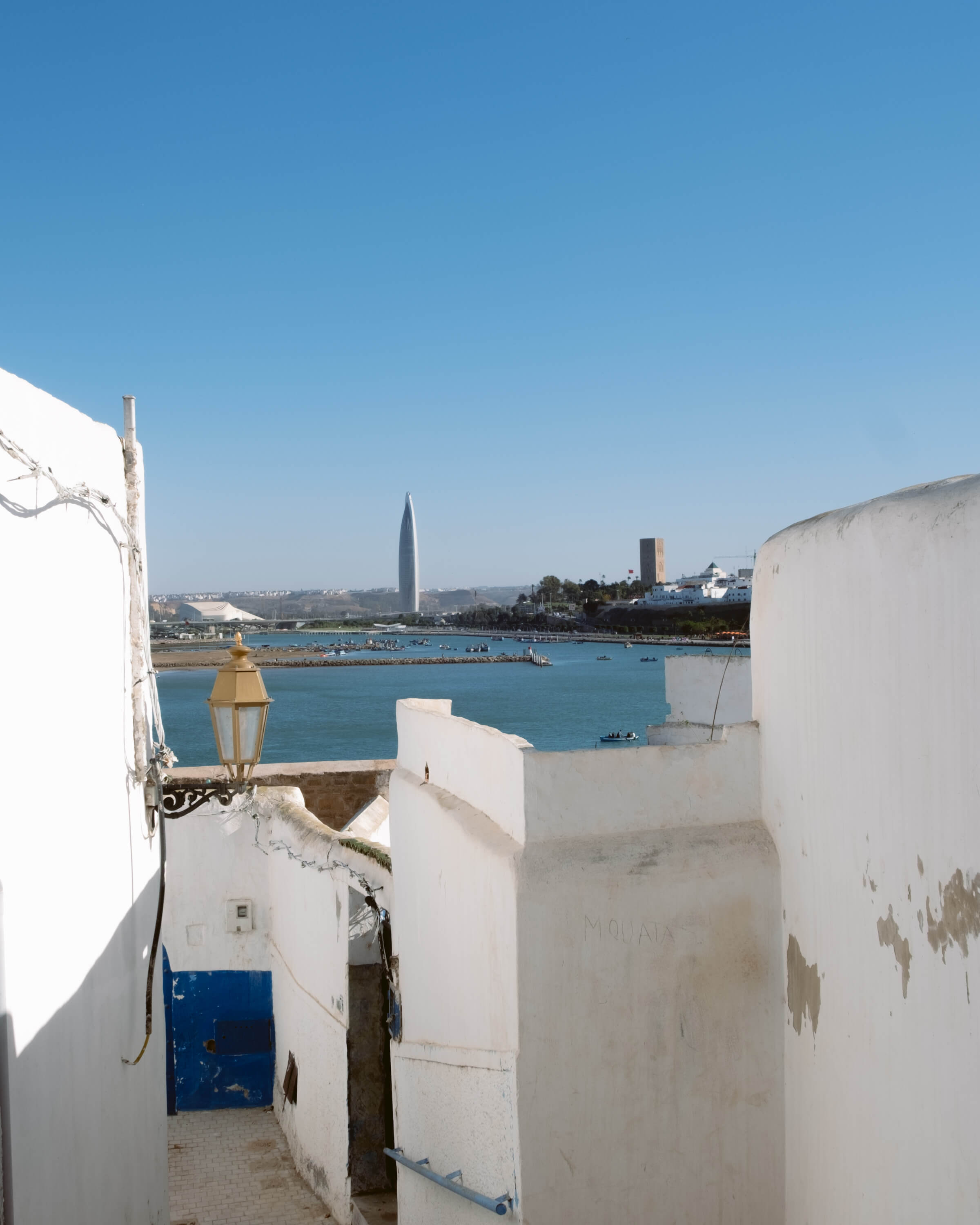 White walls of Kasbah overlook blue harbor with tall tower in Rabat, Morocco
