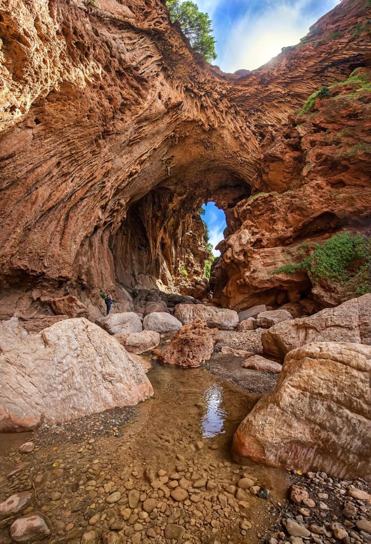 Rocky canyon with natural arch and stream flowing through rugged landscape