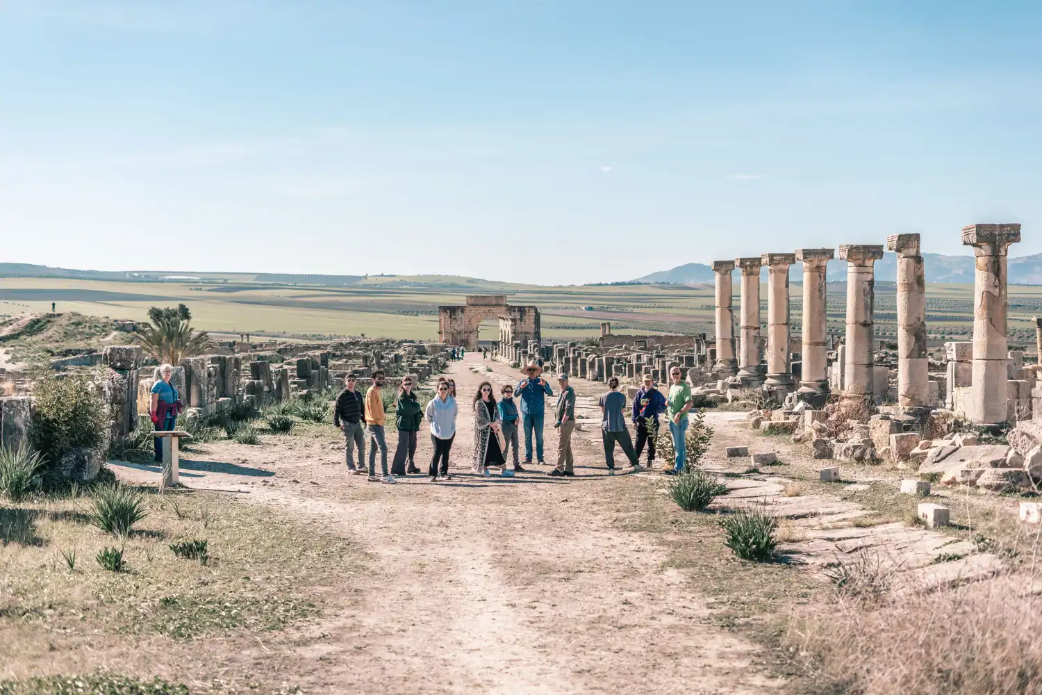 Tourists exploring ancient Roman ruins of volubilis with stone columns in desert landscape during a tour with Moroccan Guides Travel