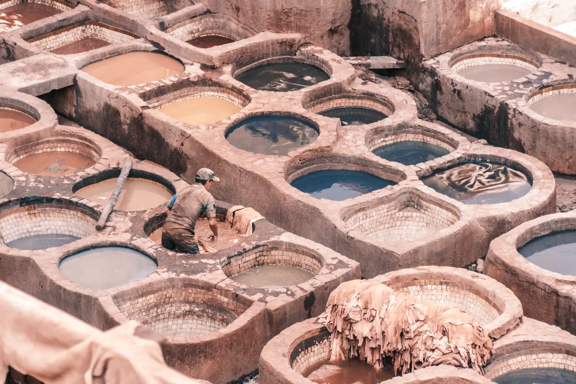 Traditional leather tannery In Fez with circular vats and worker processing hides during a tour with Moroccan Guides Travel