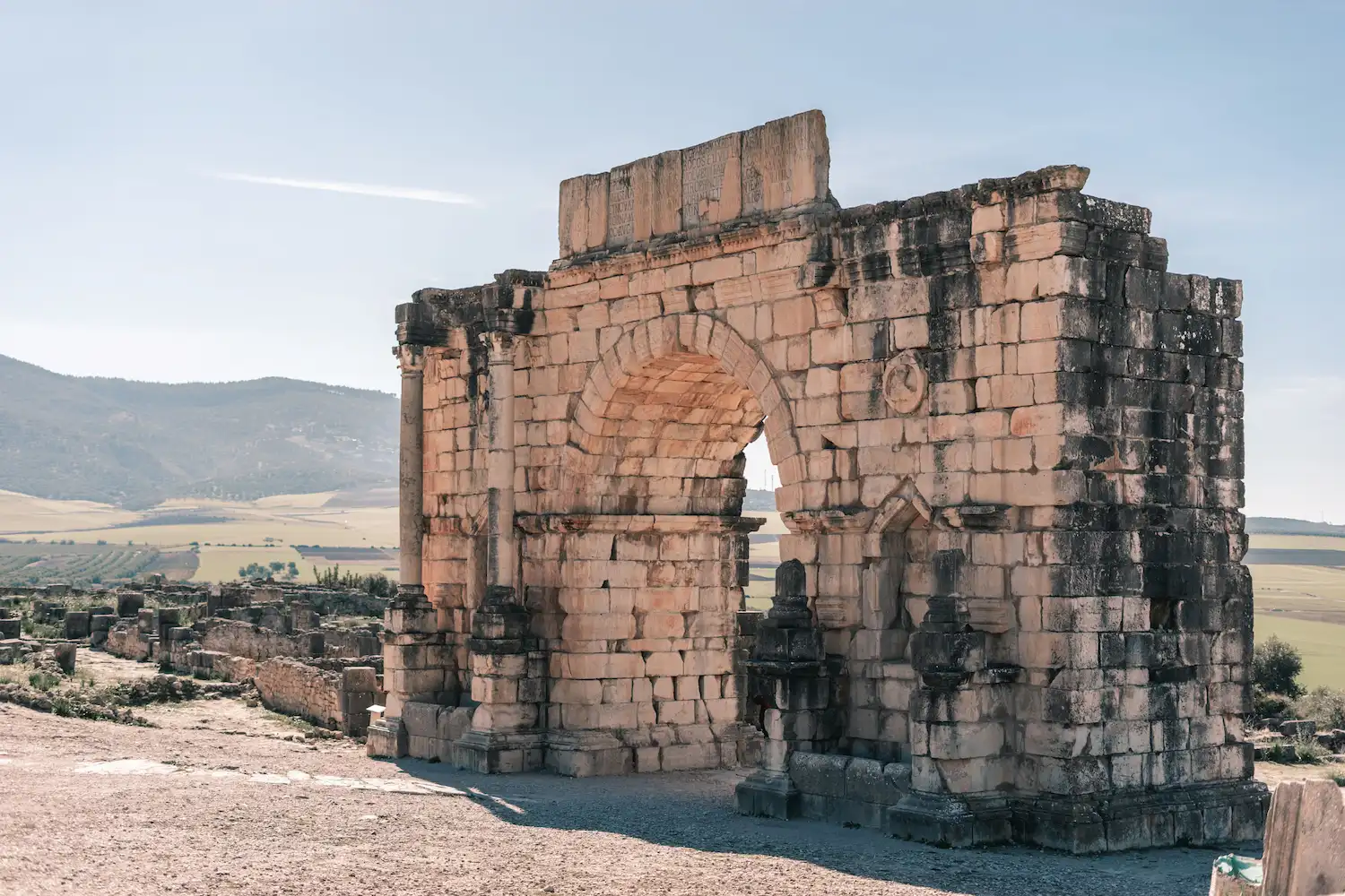 Ancient Roman stone arch Volubilis ruins with Atlas mountains in background during a guided tour Moroccan Guides travel