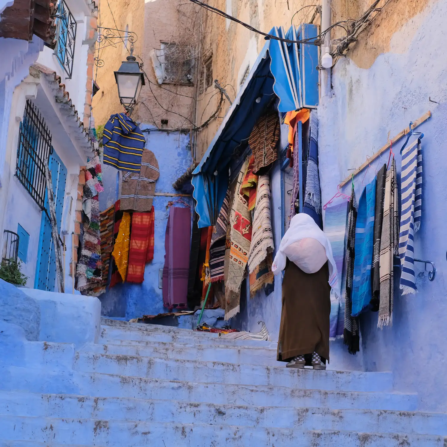 Blue-walled Moroccan street with colorful textiles and a figure walking