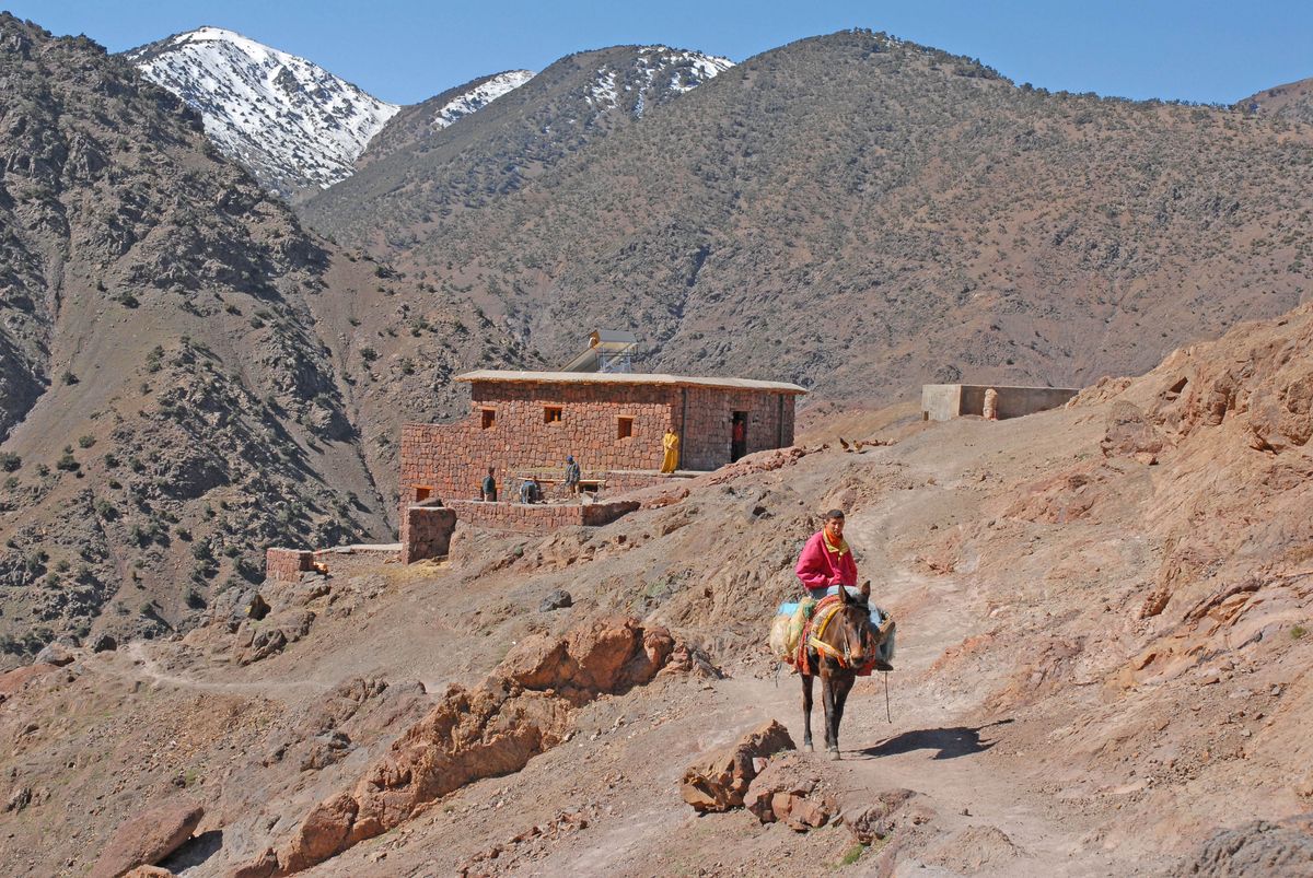 Rider on horse traversing rocky Atlas mountains path with stone building