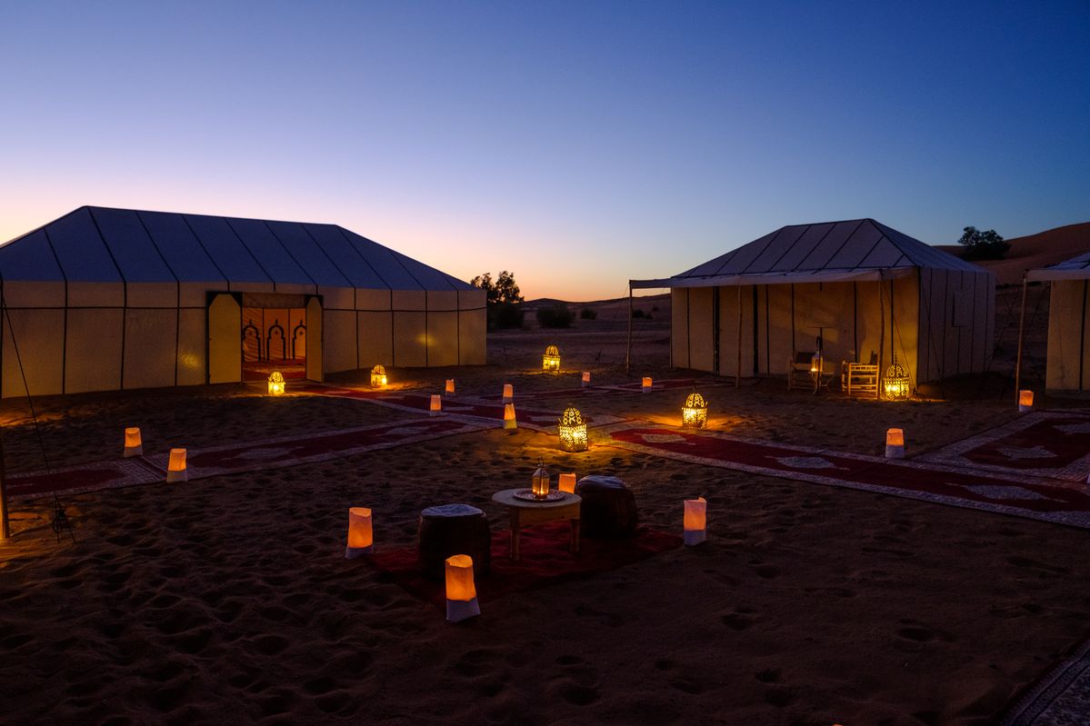 Desert camp with glowing lanterns at twilight, white tents and warm lighting