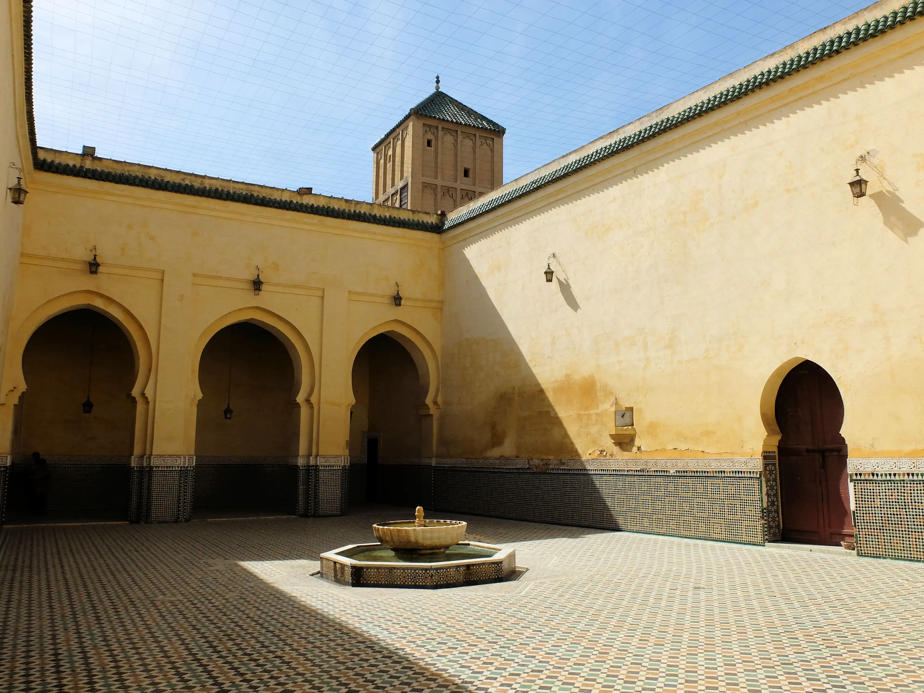 Moroccan mosque courtyard in Fes with ornate fountain, arched doorways, and tiled floor during a guided tour with Moroccan Guides Travel