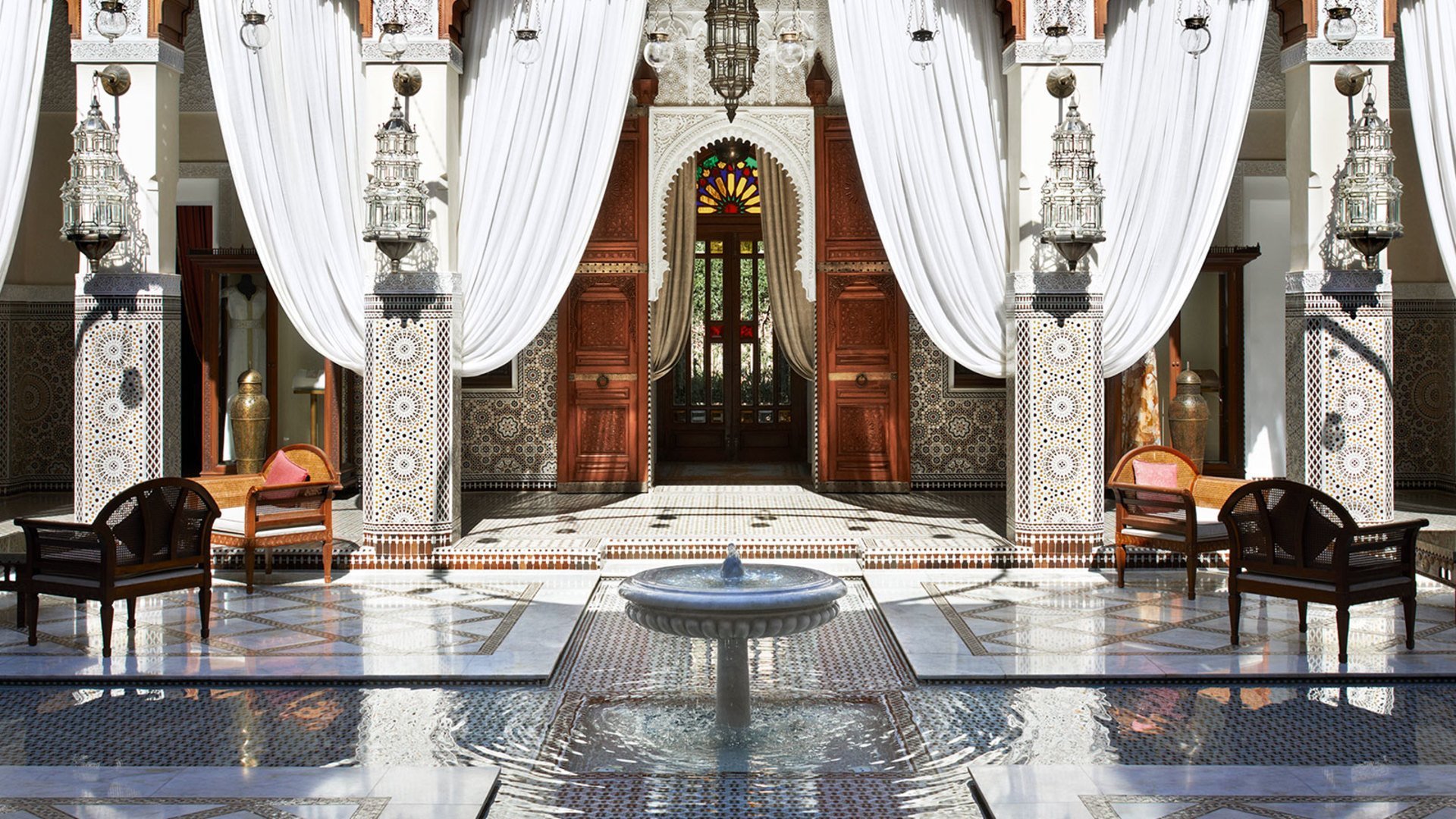 Ornate Moroccan interior with white curtains, mosaic columns, and central fountain