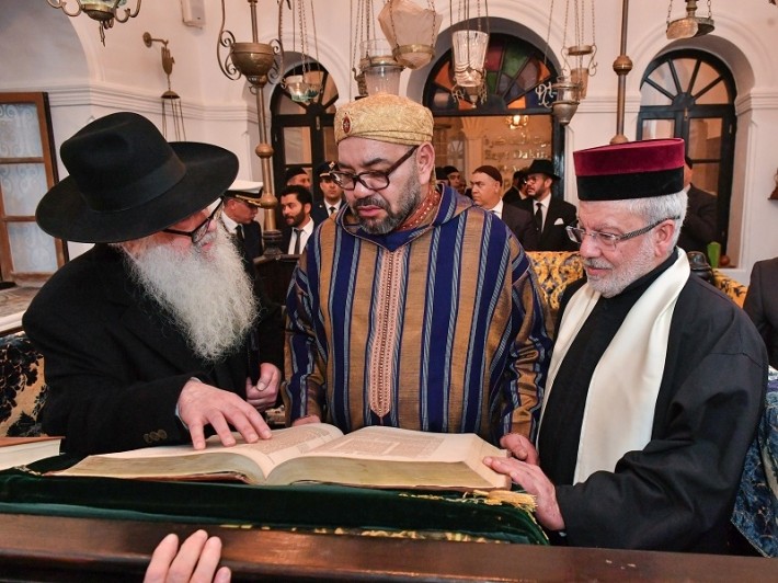 King Mohammed VI of Morocco examining a historic religious manuscript alongside Jewish community leaders on a heritage journey with Moroccan Guides Travel.