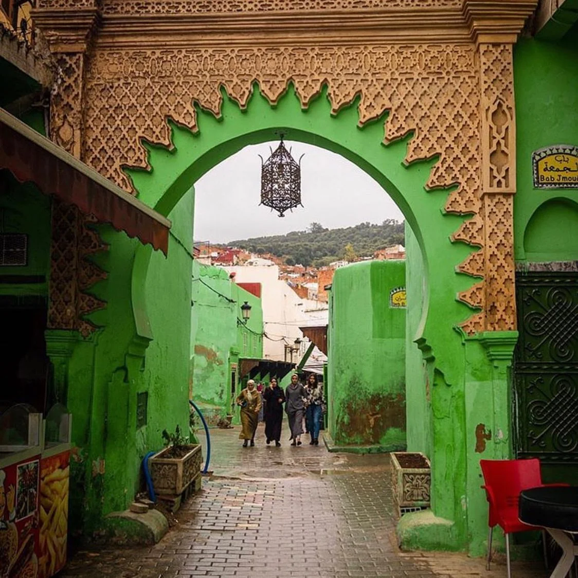 Travelers walking through a vibrant green arched gateway down a traditional street in Morocco with Moroccan Guides Travel.