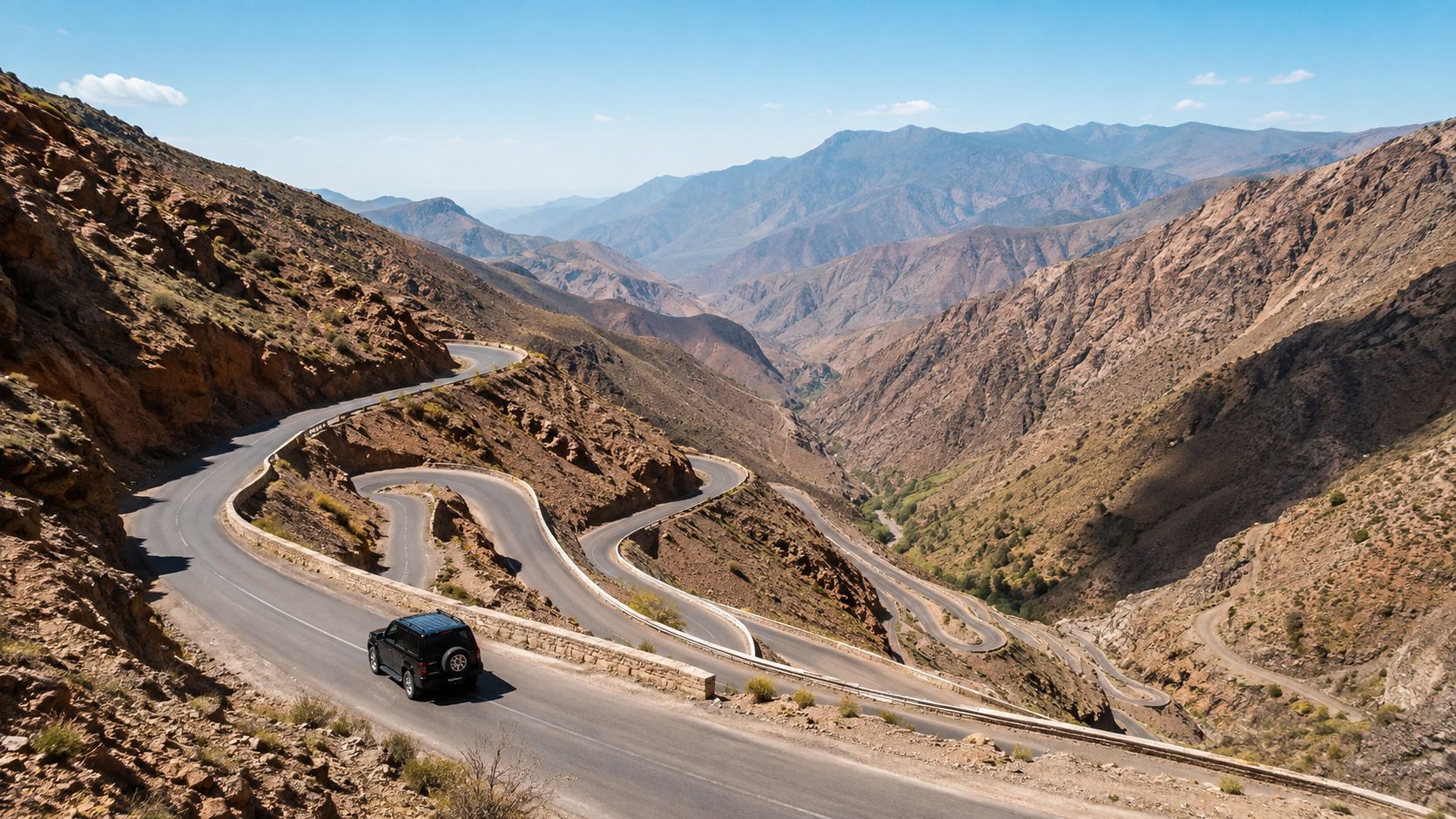 A black SUV driving down a winding mountain pass road in the Atlas Mountains of Morocco