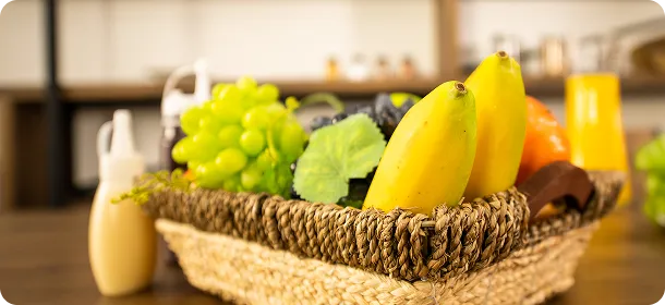 Woven basket filled with bananas, green grapes, leaves, and an orange on a wooden table.