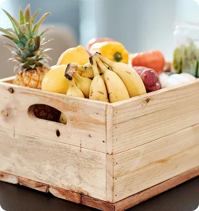 Wooden crate filled with bananas, pineapple, lemons, and other assorted fruits and vegetables.