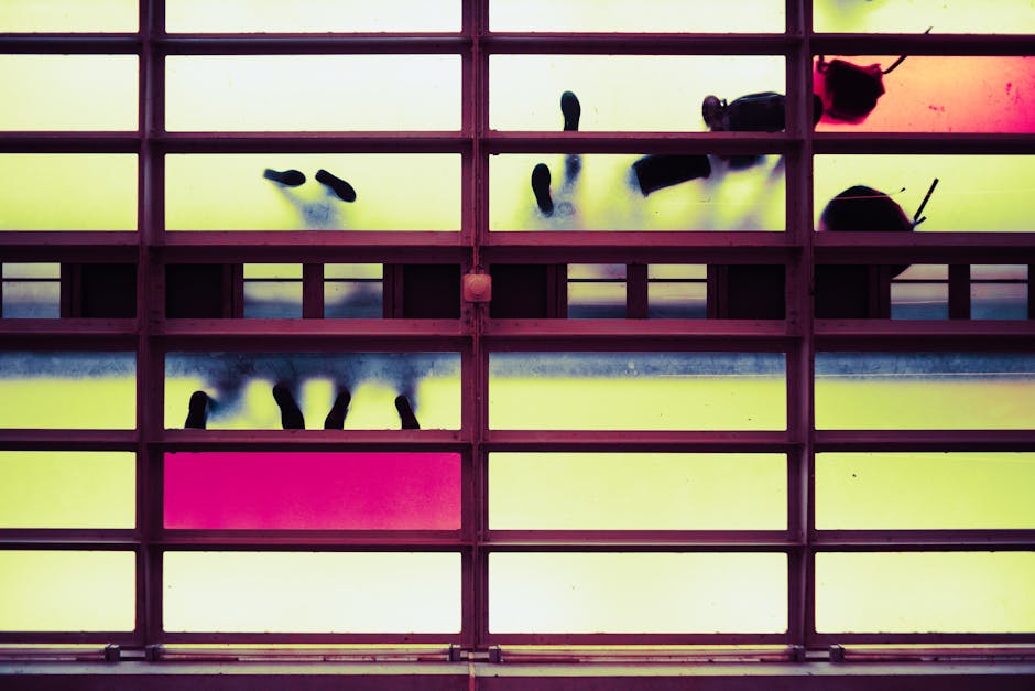 Silhouettes of people walking on a colorful glass floor, viewed from below, create an abstract and modern visual.