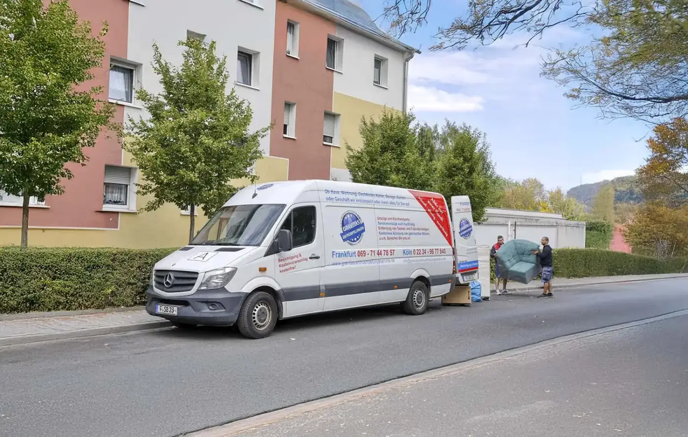 Zwei Männer heben ein grünes Sofa neben einem weißen Mercedes Transporter, der am Straßenrand vor einem Wohngebäude mit Bäumen und einer Hecke geparkt ist.
