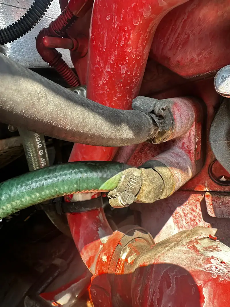 Hydraulic hose repair showing worn hose and clamp connection on heavy-duty engine with visible residue and corrosion.