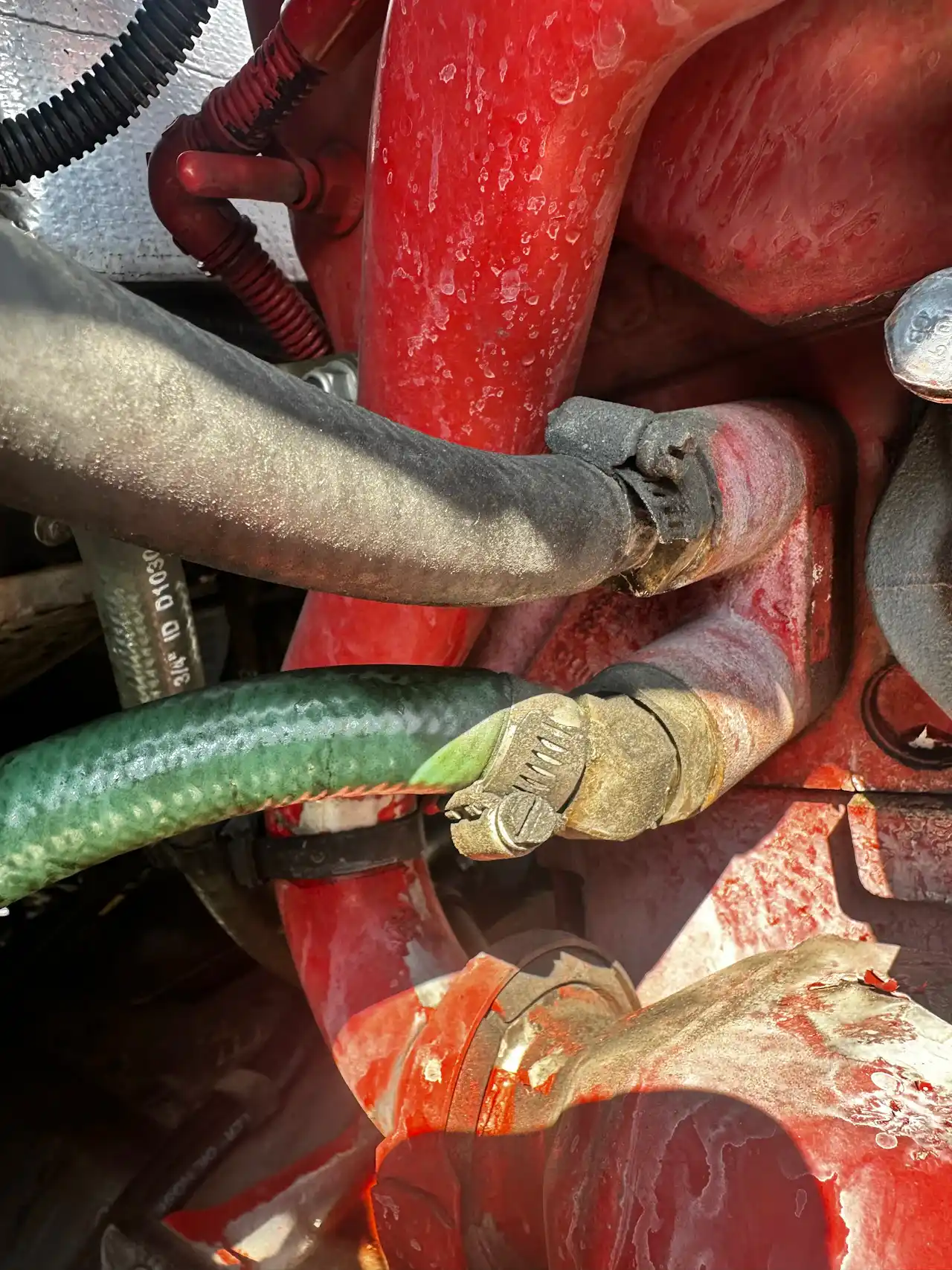 Hydraulic hose repair showing worn hose and clamp connection on heavy-duty engine with visible residue and corrosion.