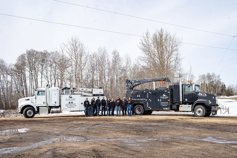 Central Alberta crew standing between two heavy-duty service trucks at a muddy worksite.