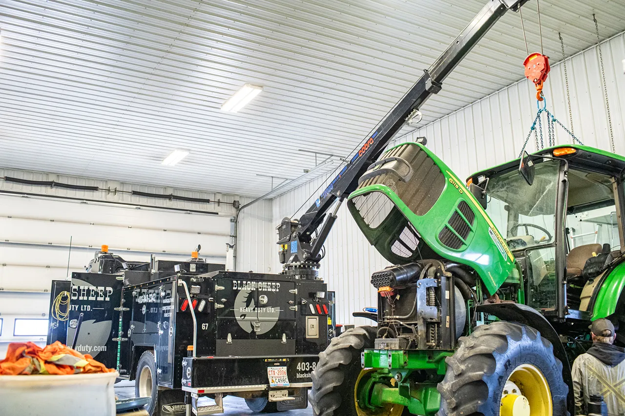Forestry equipment tractor under crane repair beside a Black Sheep Heavy Duty Ltd. service truck.