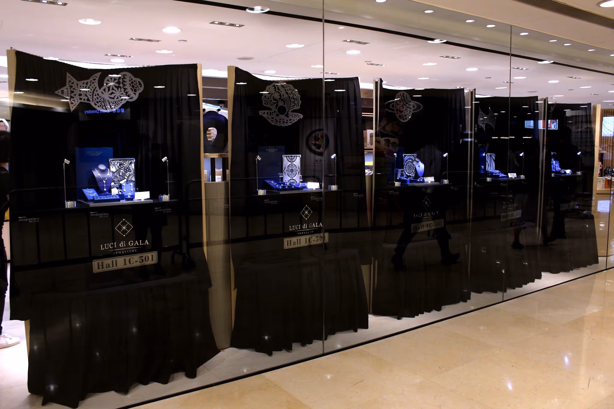 Jewelry store display cases with blue-lit jewelry pieces behind glass and black curtains, labeled LUCI di GALA Hall 1C-501.