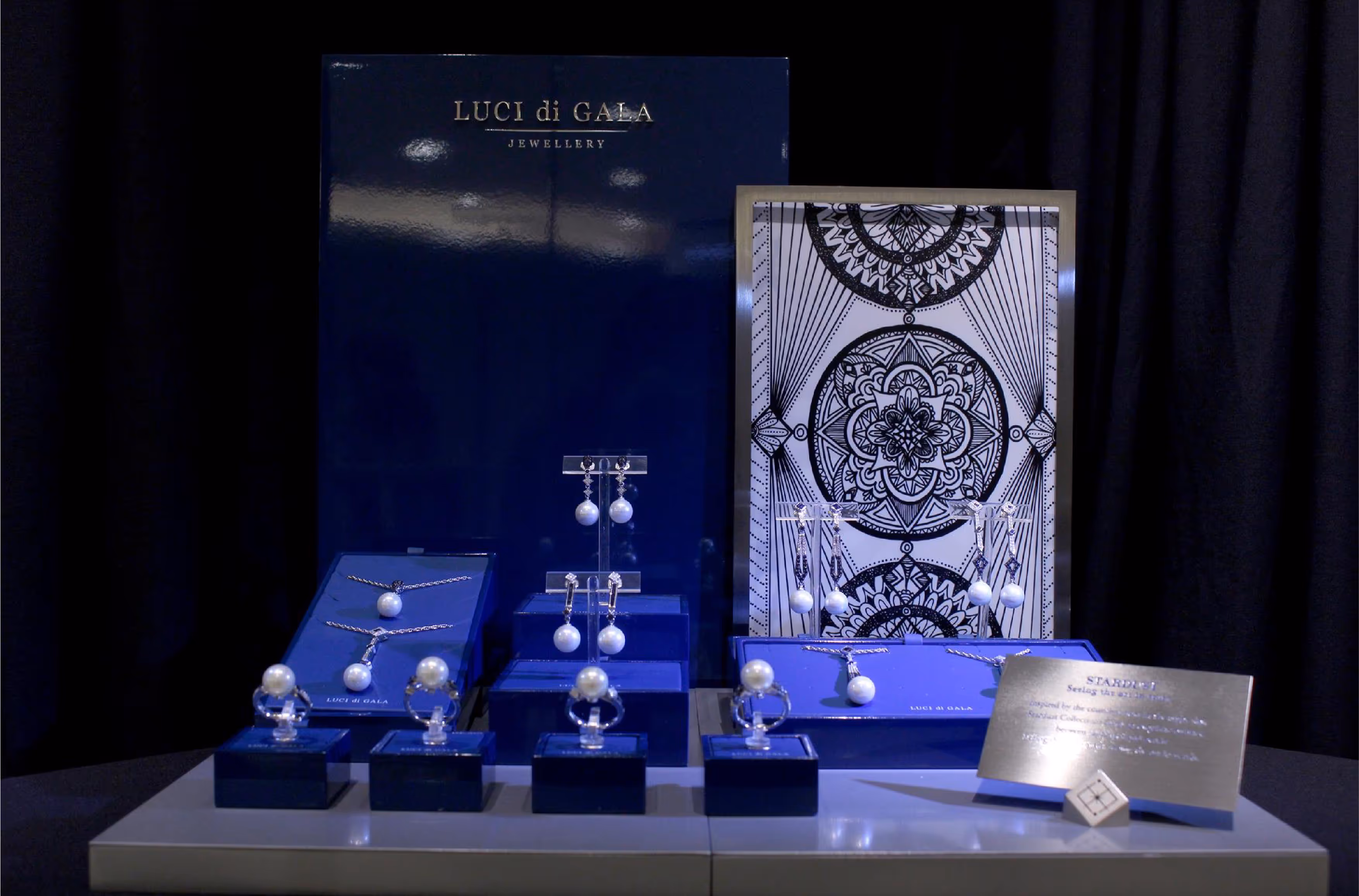 Luci di Gala jewellery display featuring pearl rings, earrings, and necklaces on blue stands with a decorative black and white backdrop.