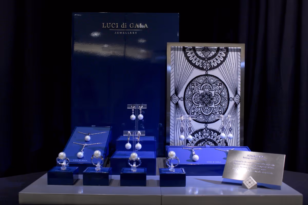Display of pearl jewelry including rings, earrings, and necklaces on dark blue stands with a dark patterned backdrop and a LUCI di GALA Jewellery banner.