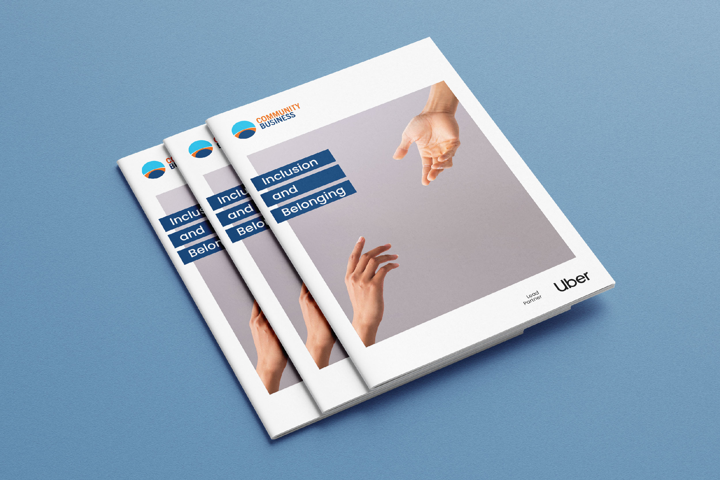 Stack of booklets titled 'Inclusion and Belonging' featuring reaching hands on the cover, with Community Business and Uber logos.