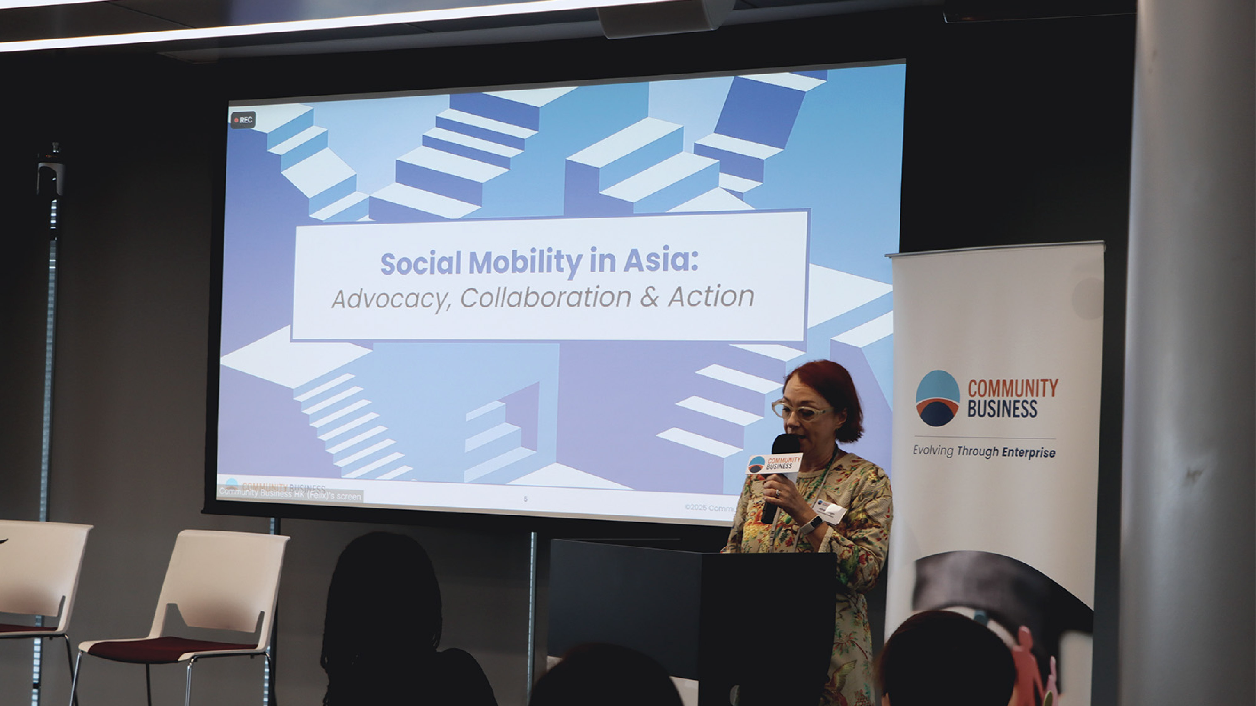 Speaker at podium with microphone in front of screen titled 'Social Mobility in Asia: Advocacy, Collaboration & Action.'