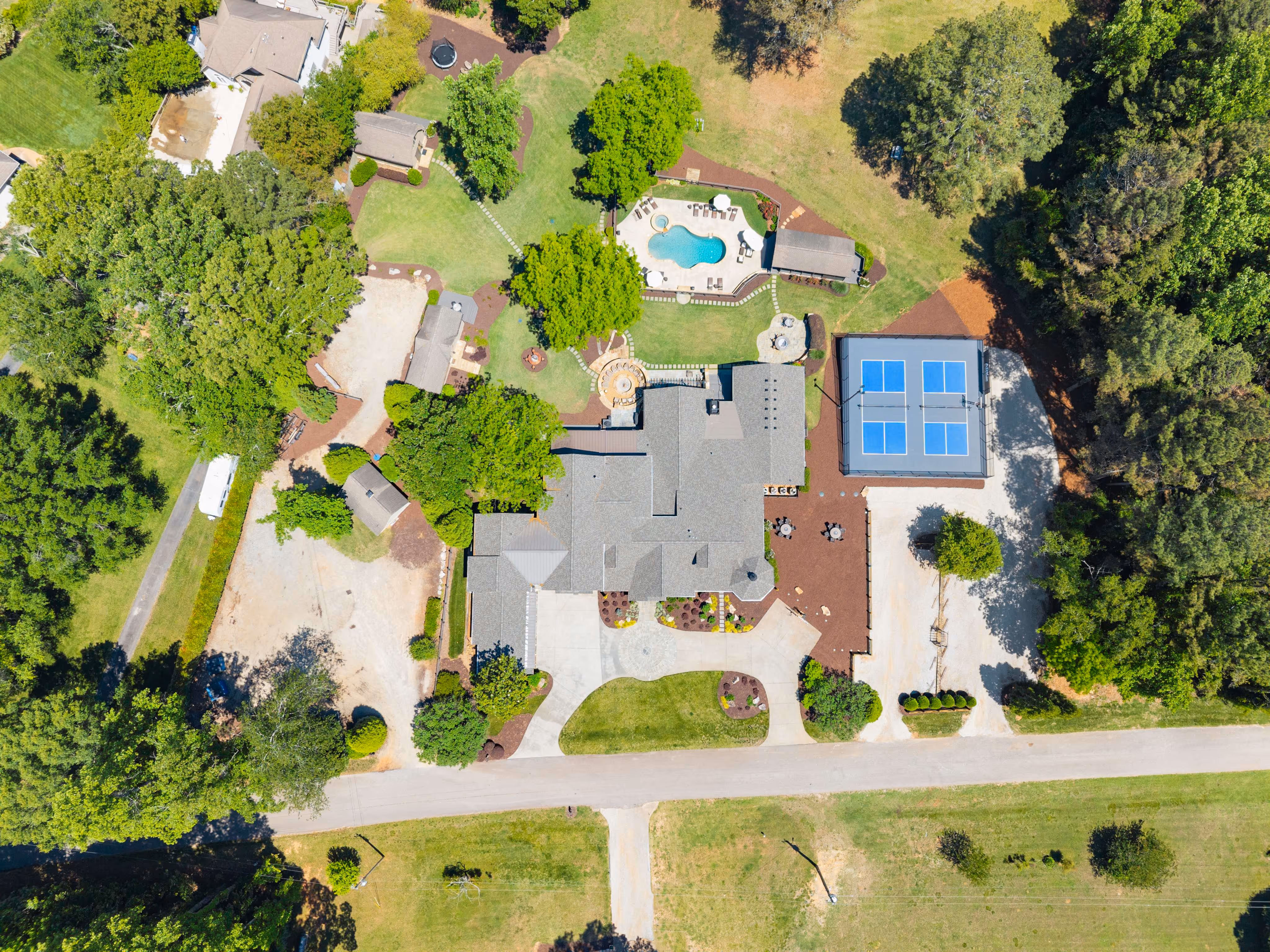 overhead drone style photo of large lake house property with pool and pickleball courts and large yard