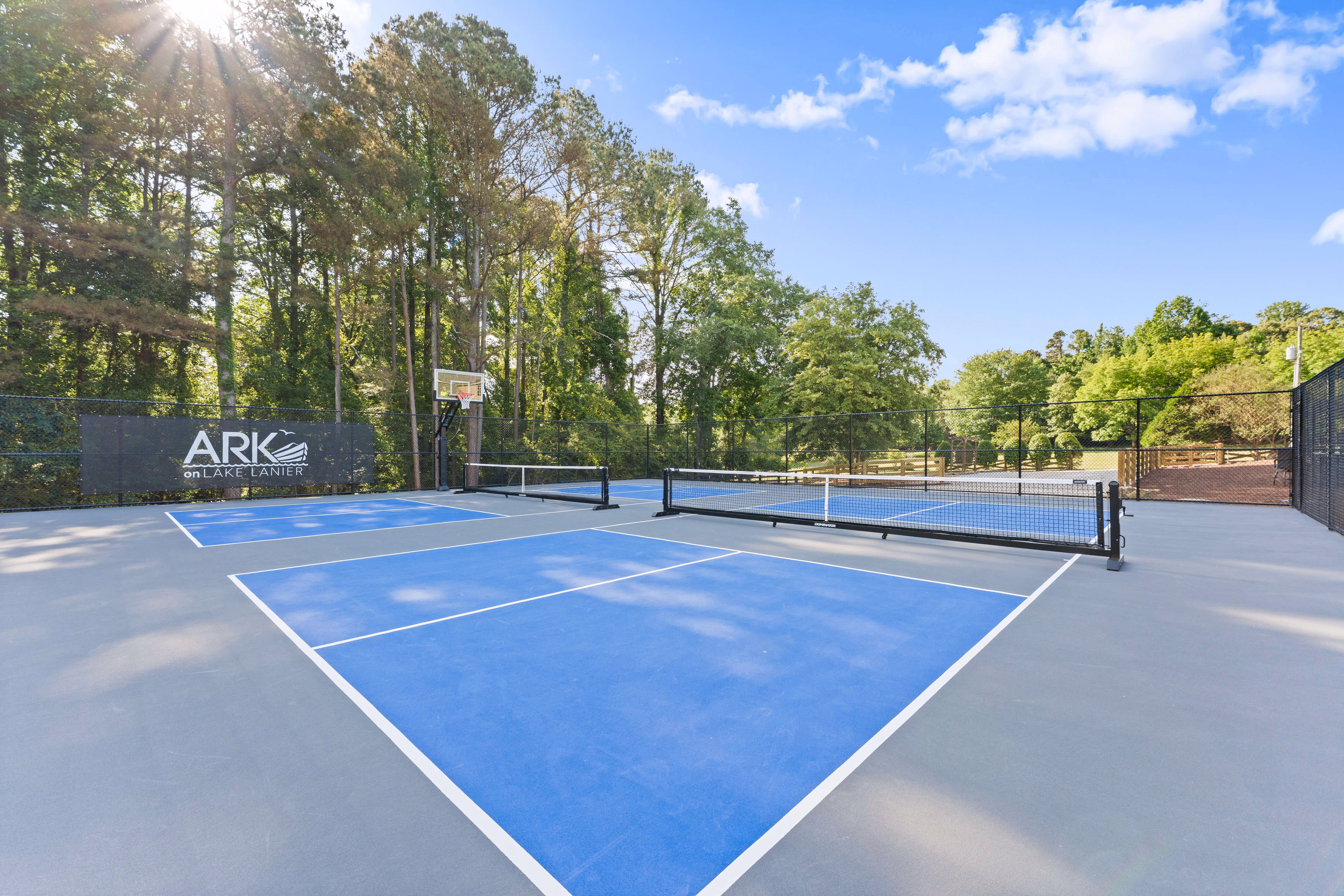 side view of pickleball and basketball court in front of wooded area
