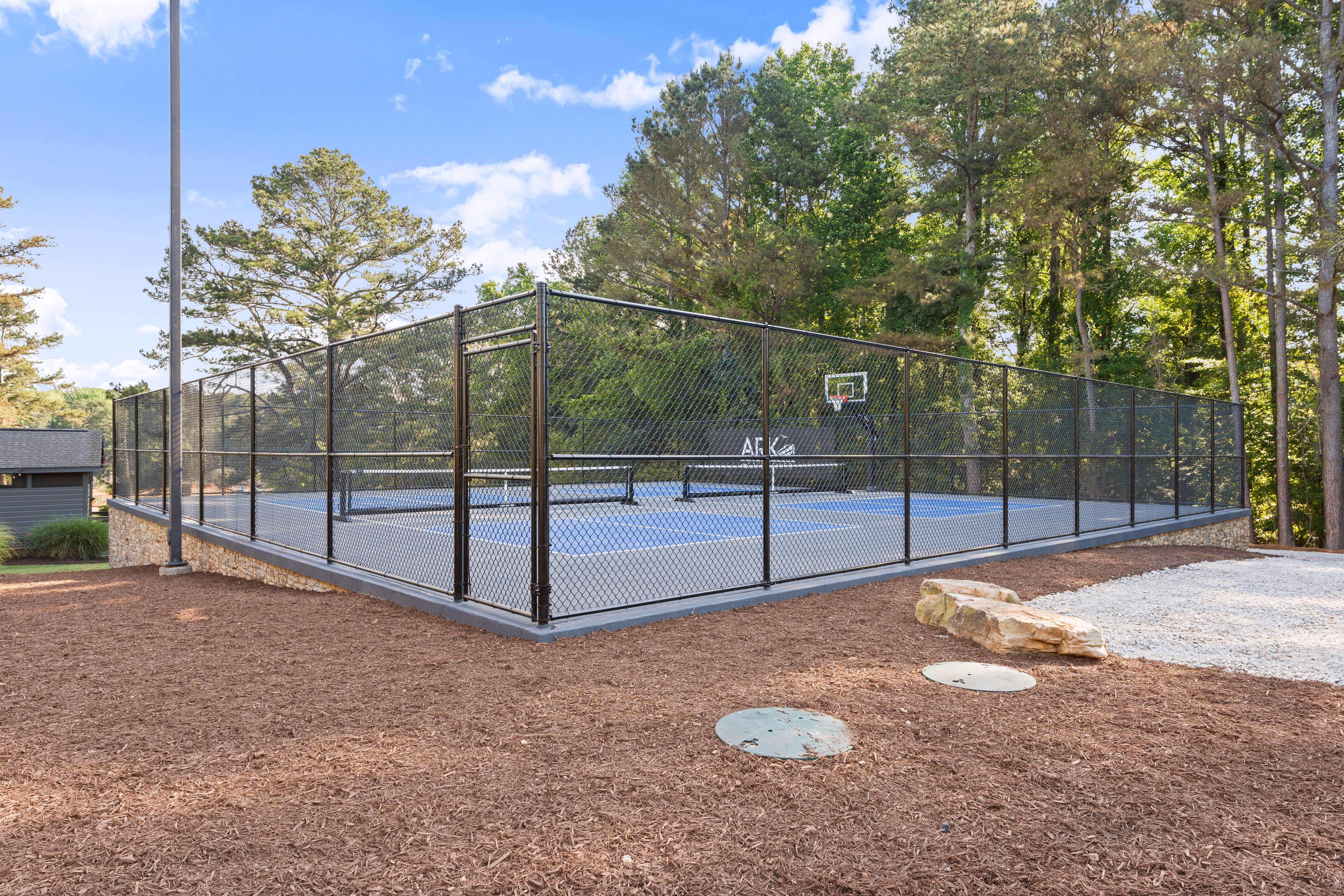 side view of pickleball and basketball court in front of wooded area