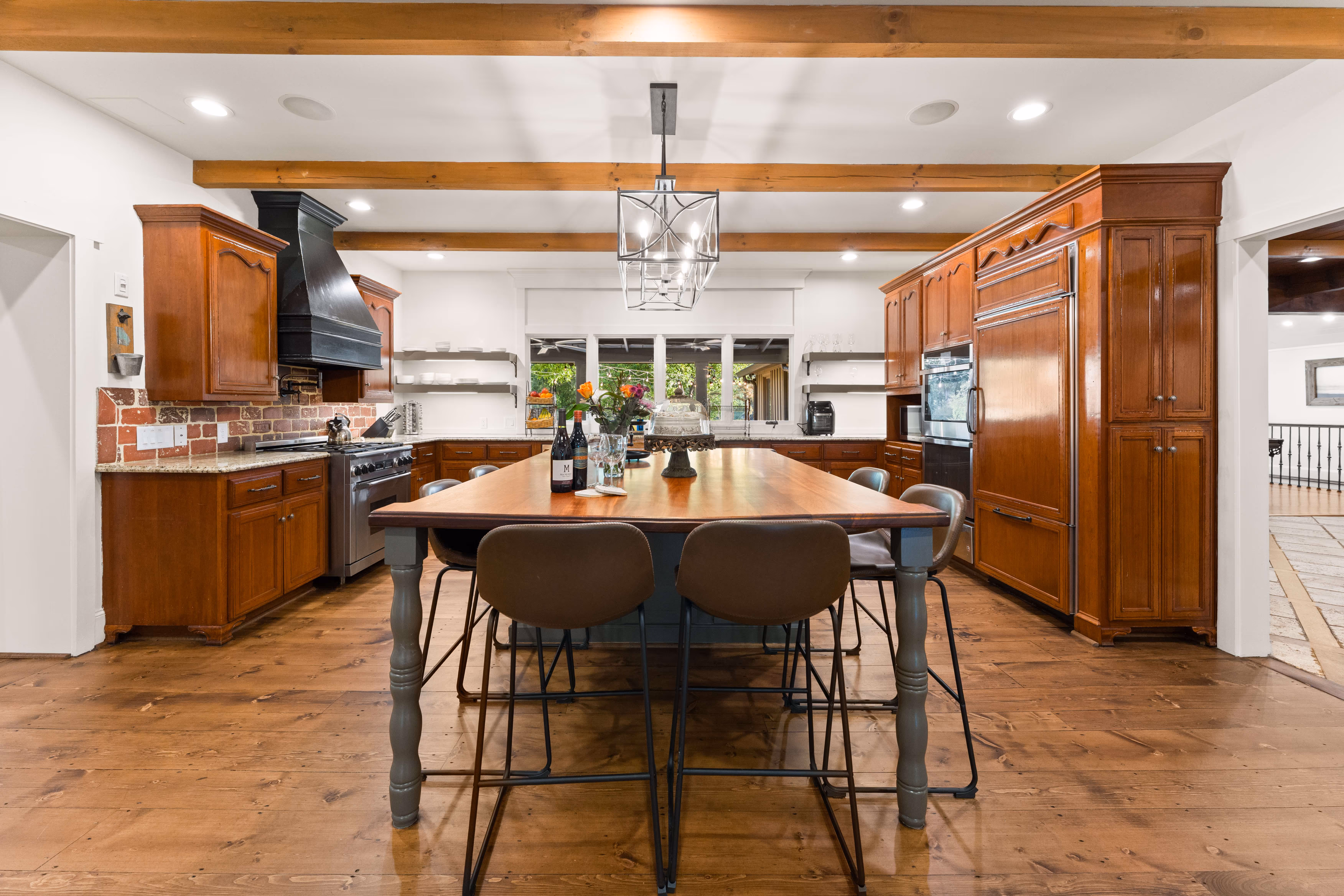 Spacious kitchen with wooden cabinets, a large island table, stools, and exposed ceiling beams.