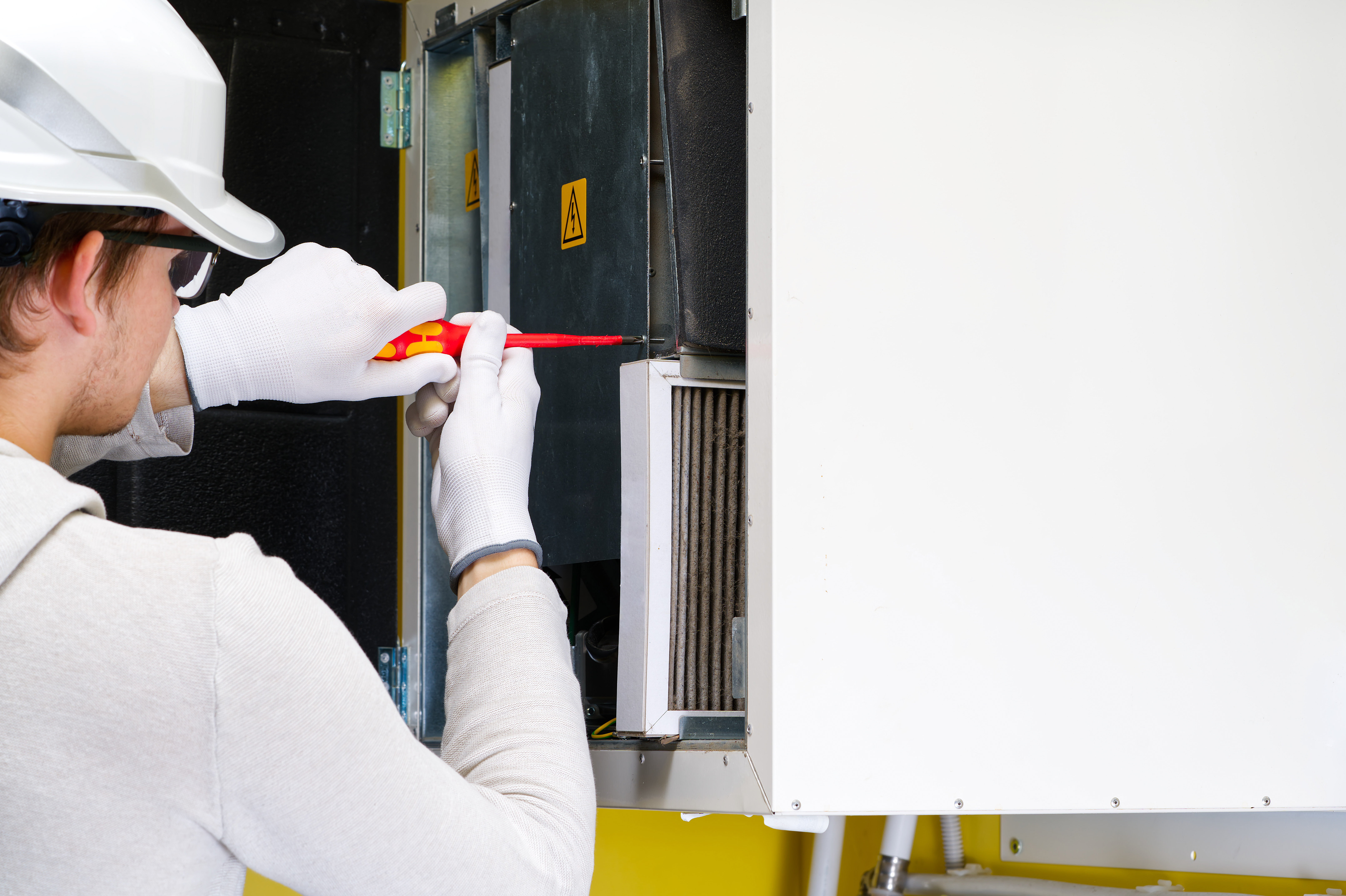 A professional HVAC technician wearing a white hard hat and safety gloves inspecting a high-efficiency furnace and preparing to replace a dirty air filter during a maintenance service call in London, Ontario.