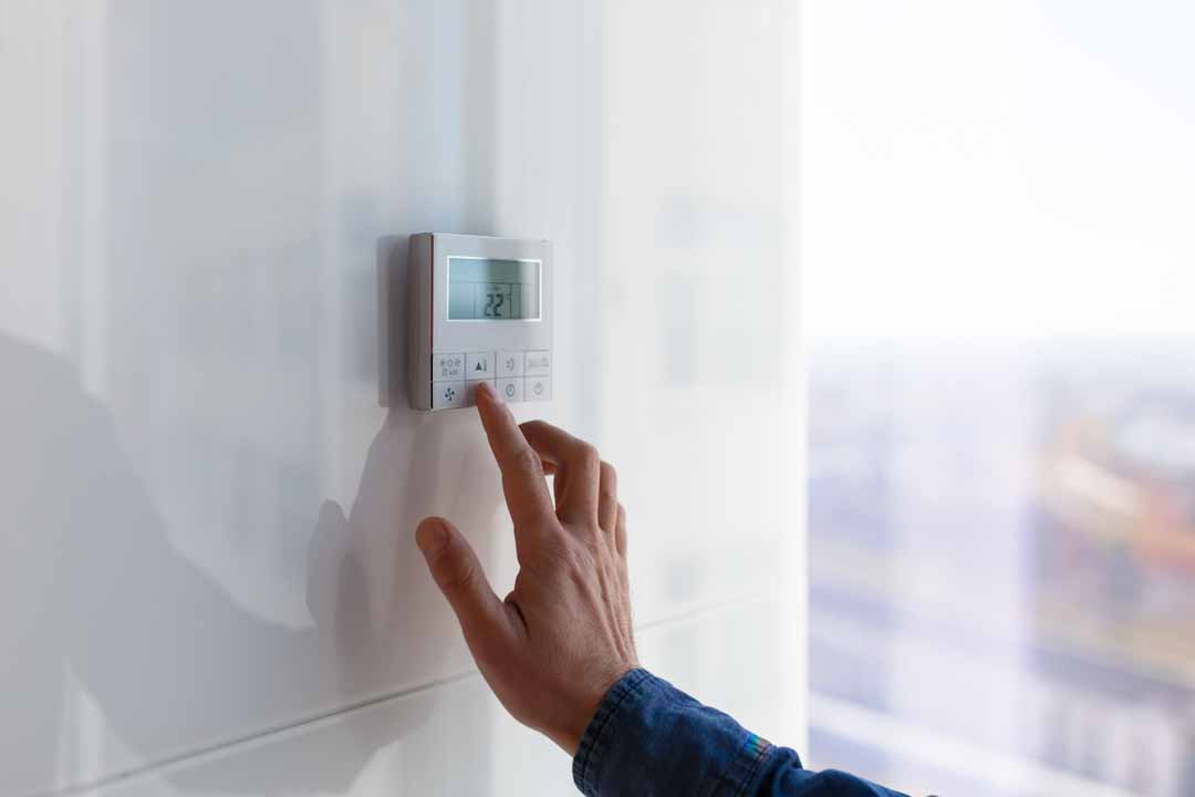 A hand changing the settings on a thermostat.