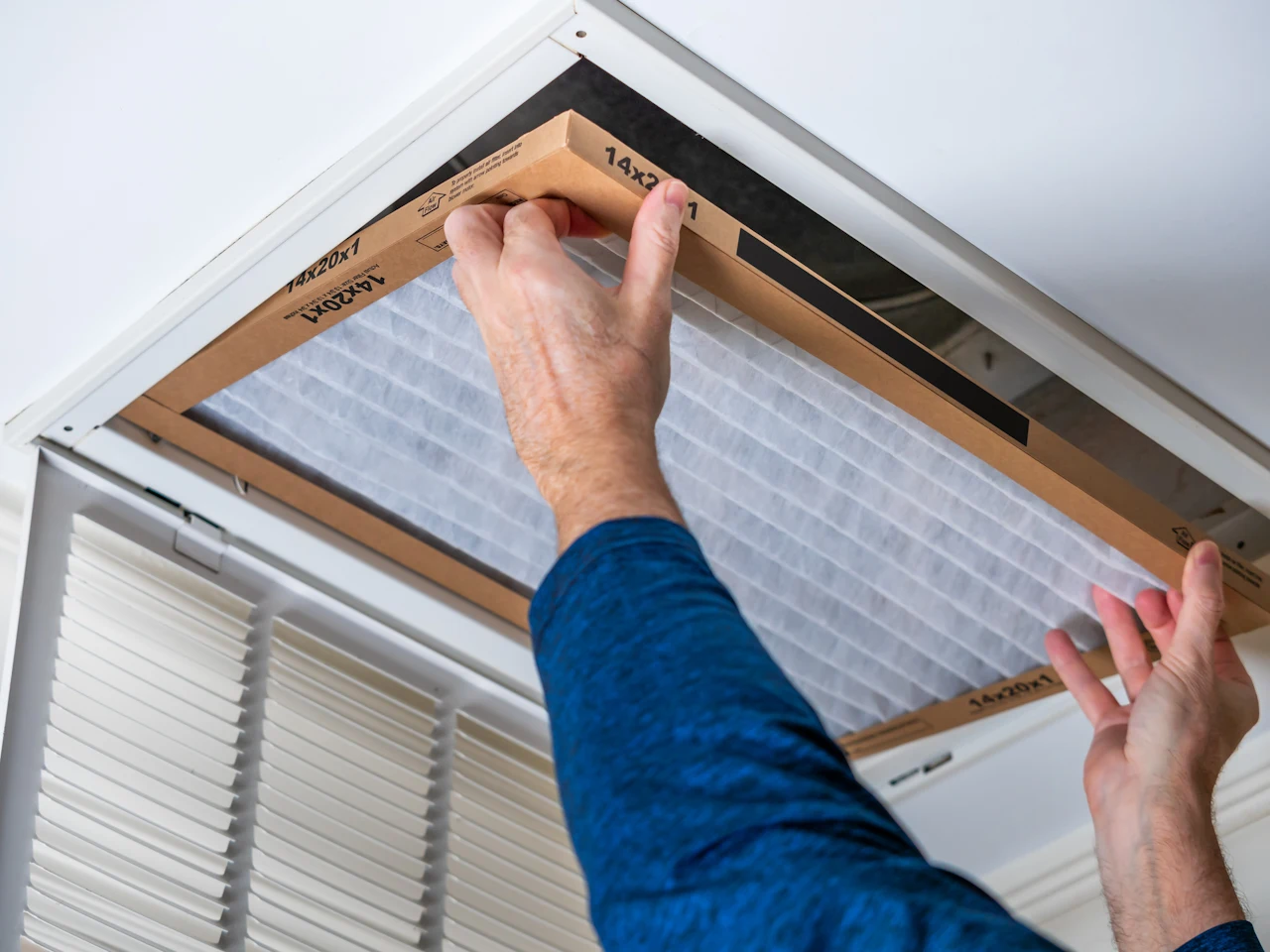 Two hands installing a new ventilation filter into a ceiling vent.