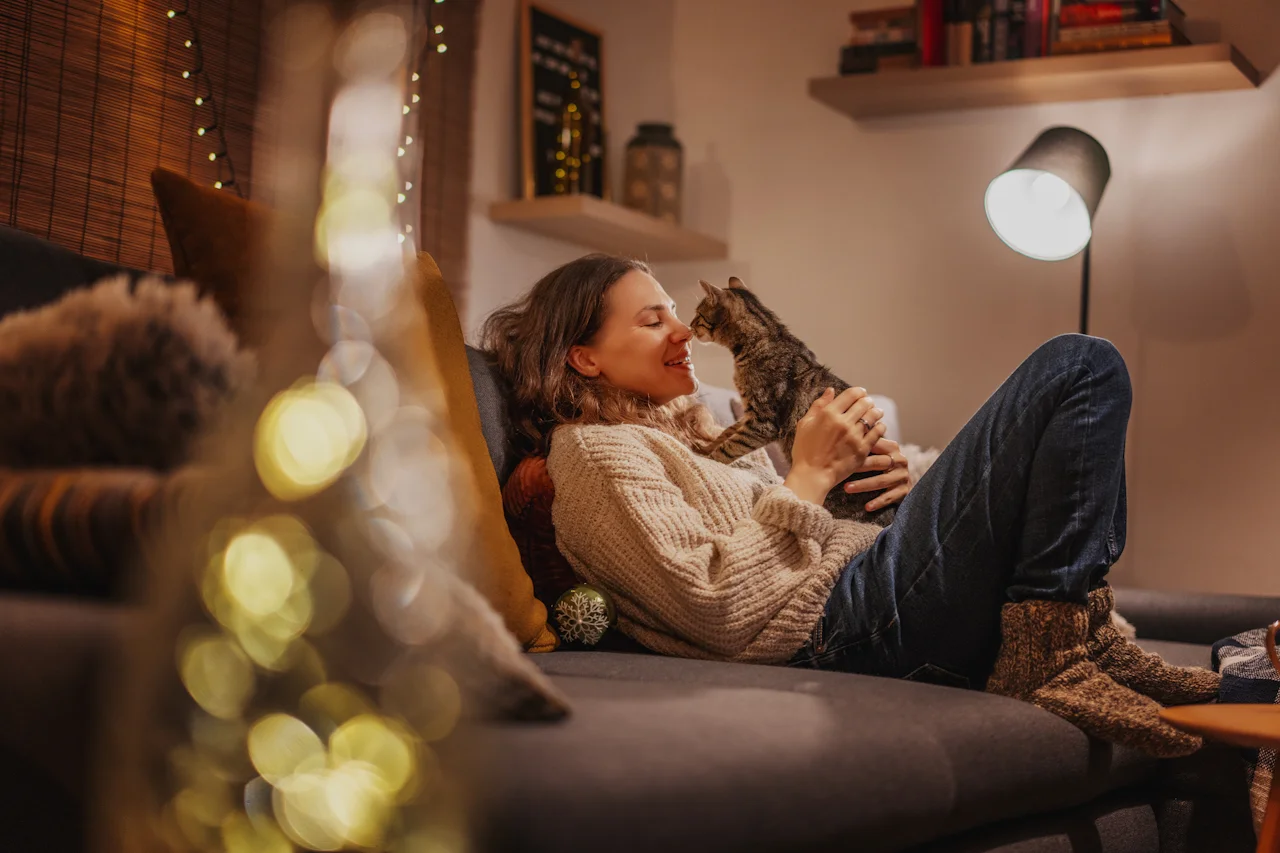 A lady wearing warm clothes sitting on a couch with a cat.