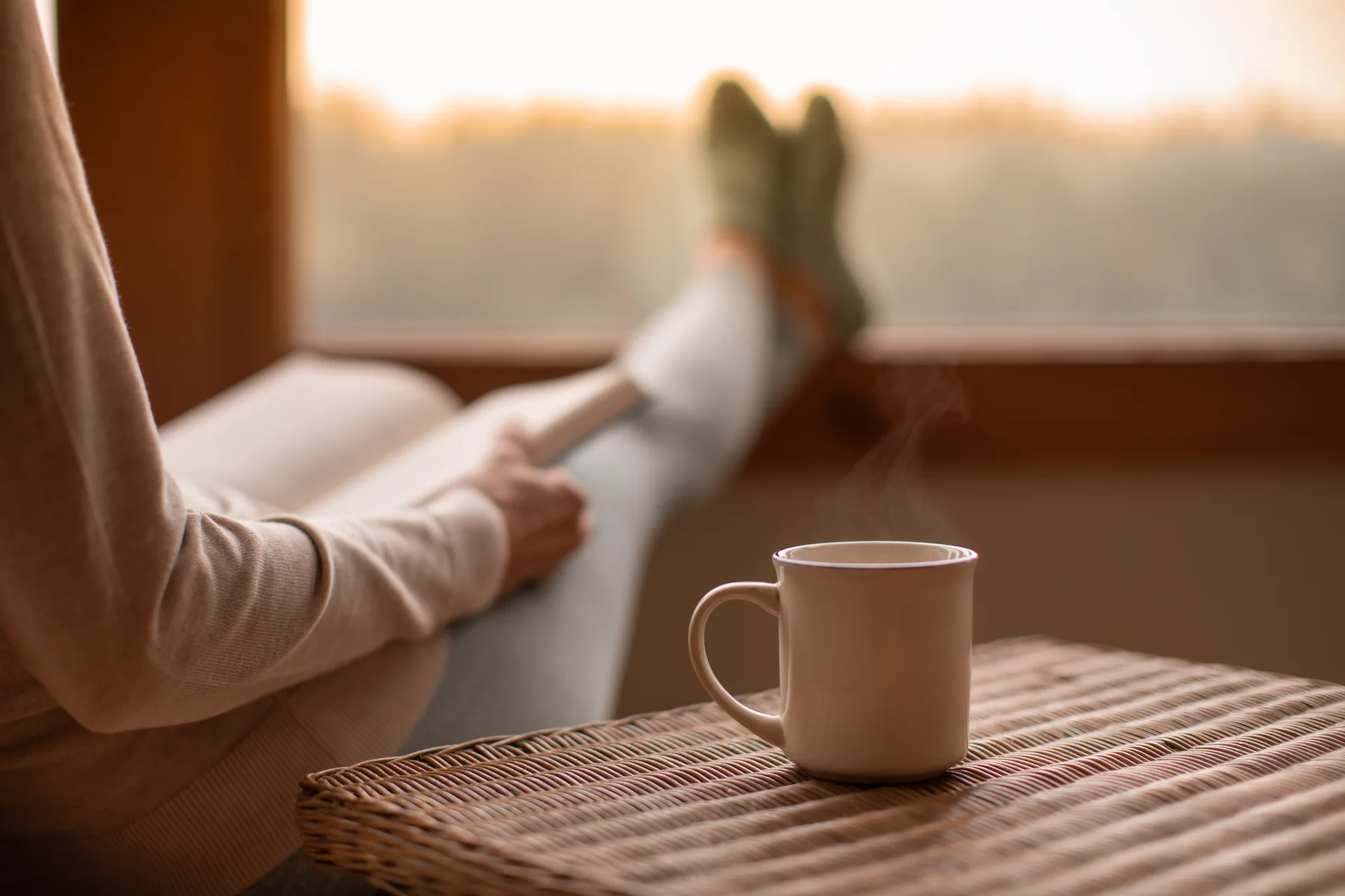 A person reading a book with a coffee next to them.