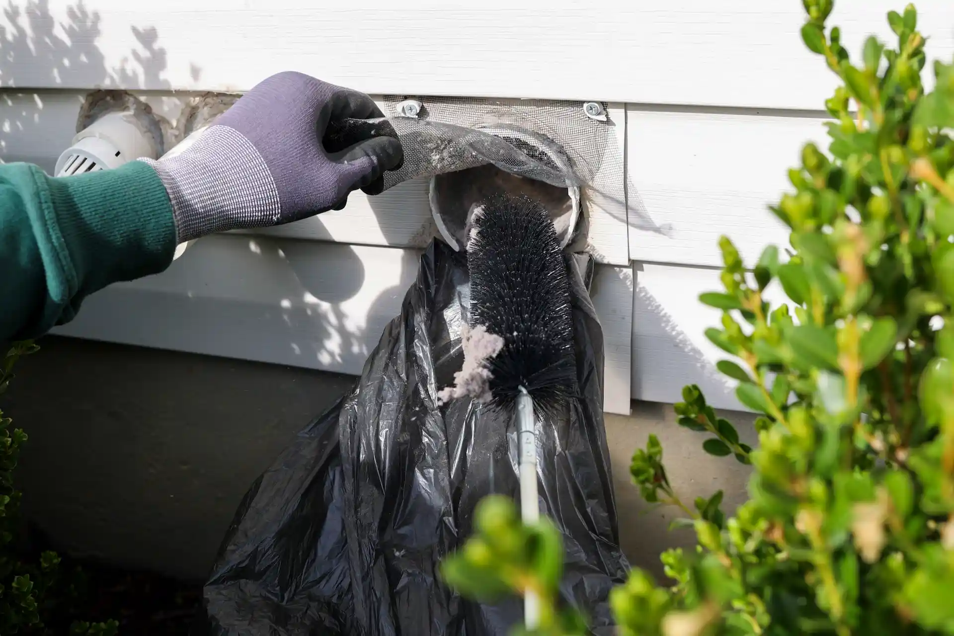 Someone cleaning their dryer lint vent on the outside of their home.