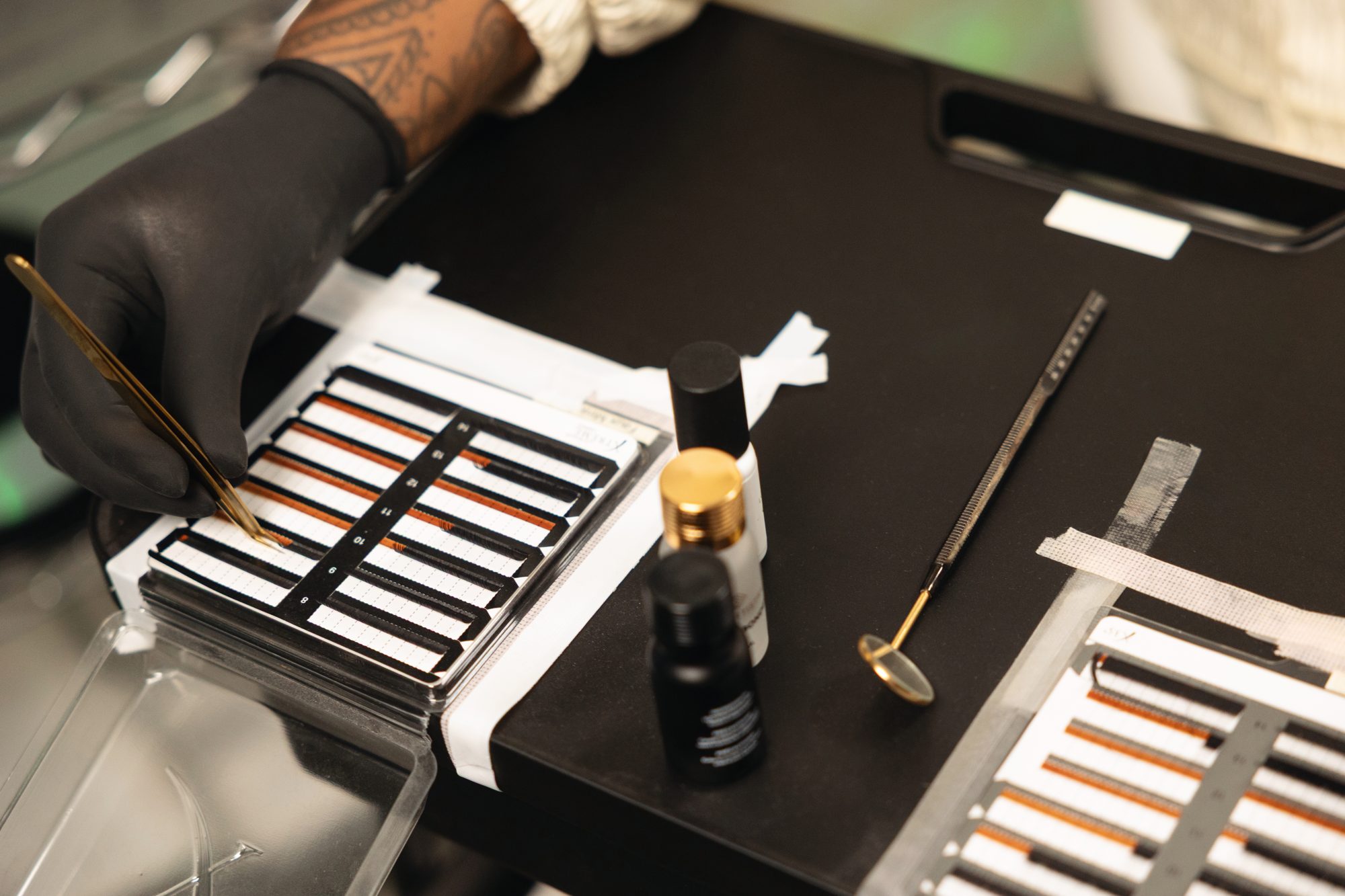 Gloved hand selecting lash extensions from a tray