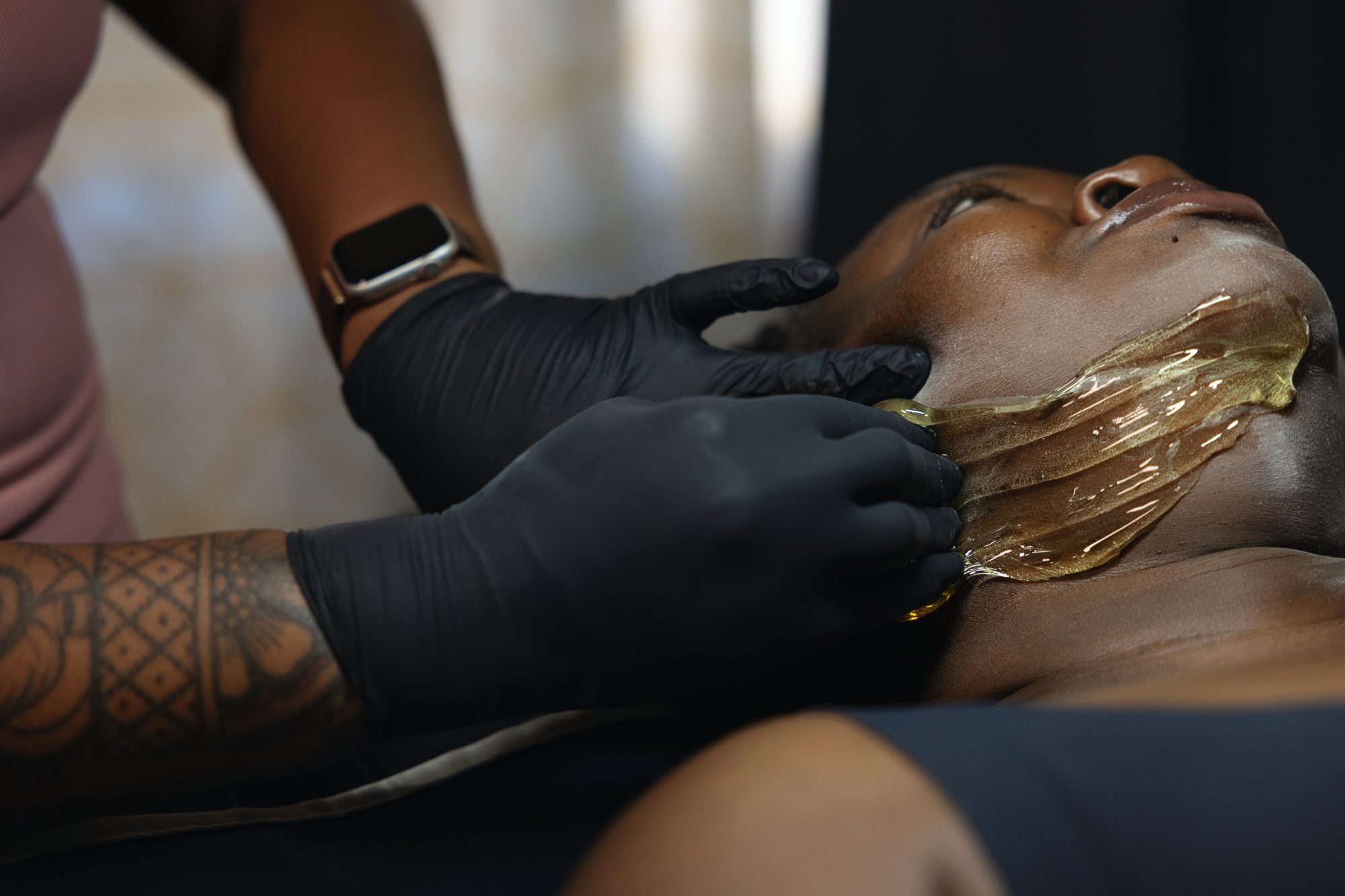 Gloved hands applying golden paste along a client's jawline at Your Bliss