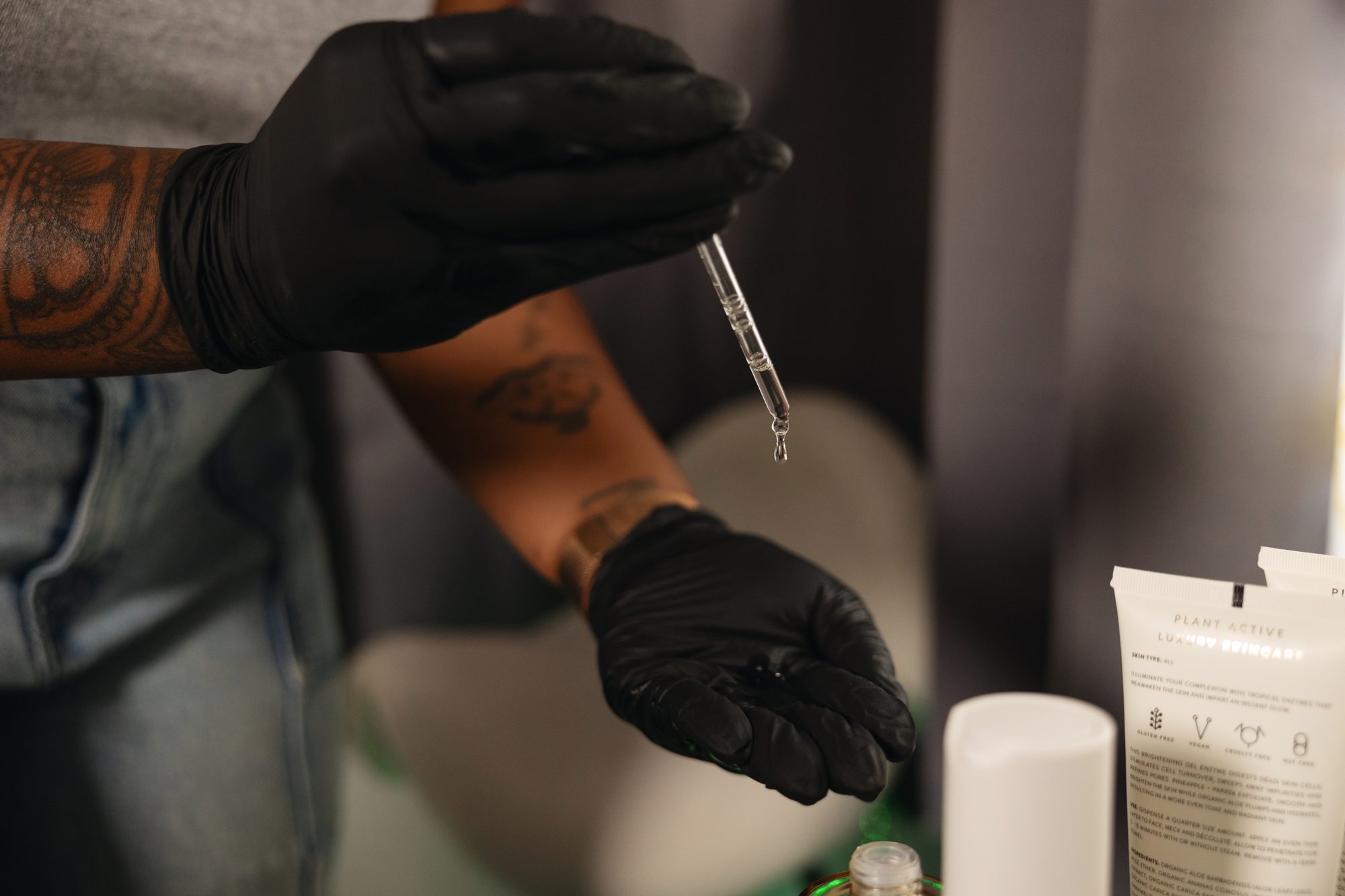 Gloved hands holding a serum dropper over skincare products