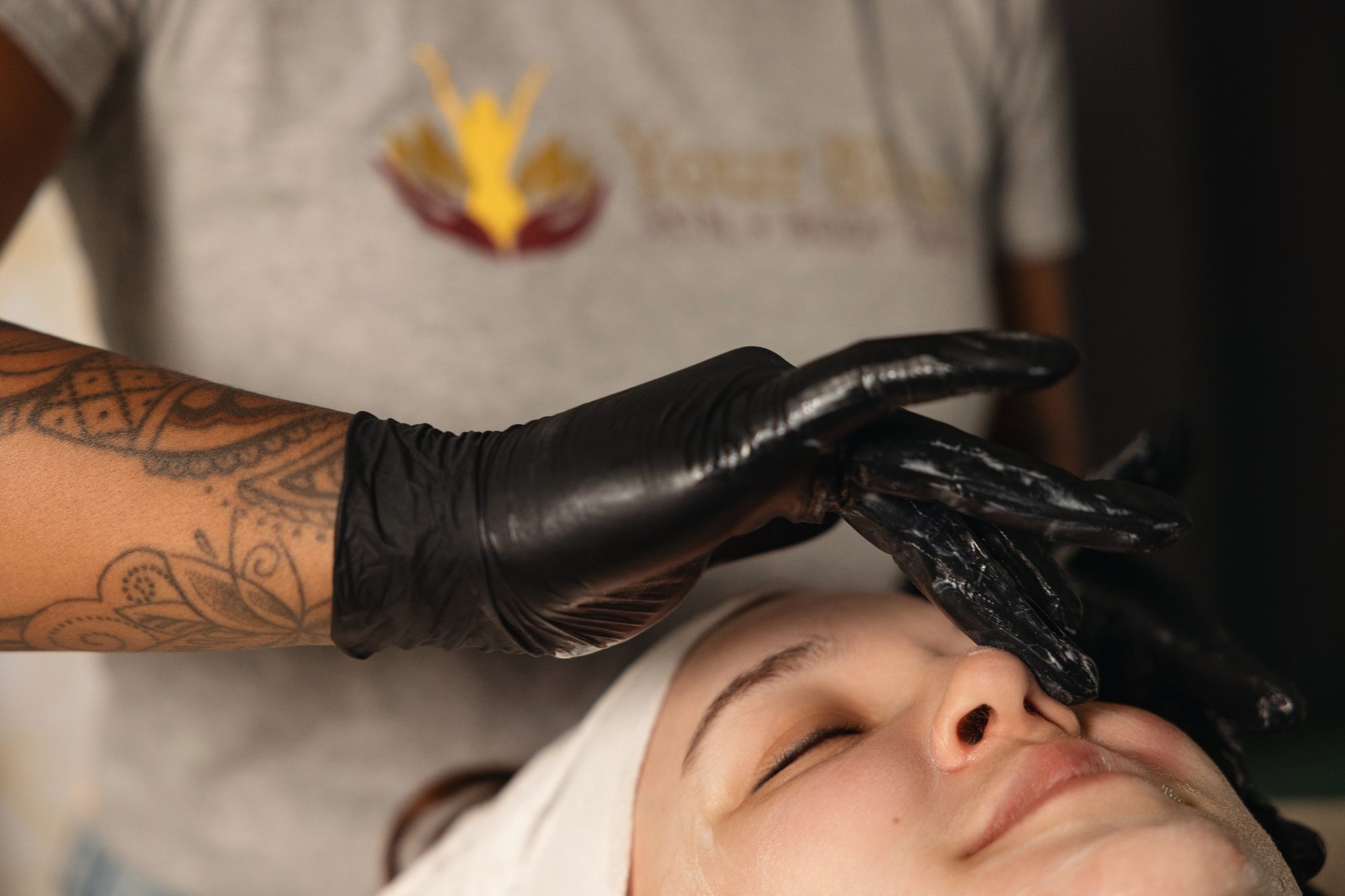 Gloved hands applying a dark mask during a facial