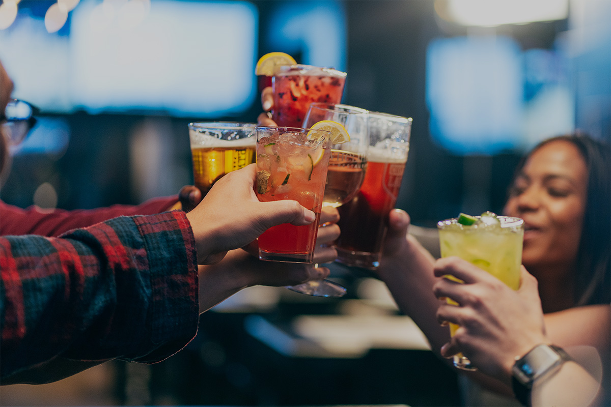 Friends toasting with colorful cocktails at a bar.