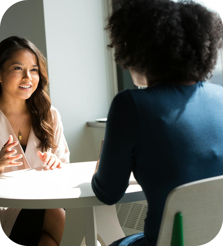 Two women engaged in a conversation while sitting opposite each other at a white table.